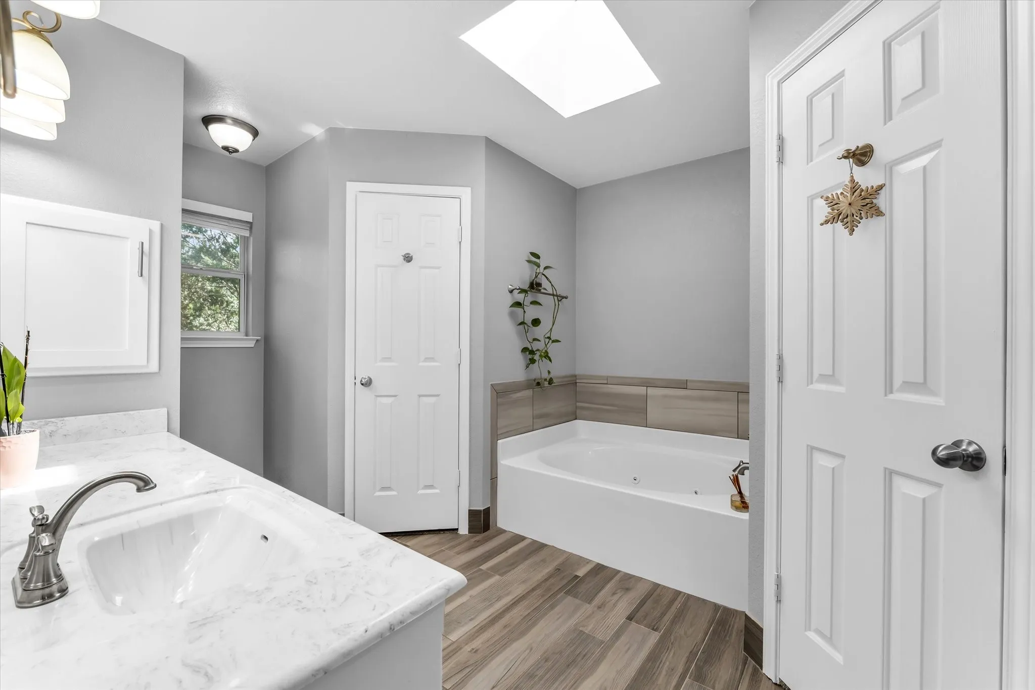 Bathroom featuring a spacious vanity with a white countertop, brushed nickel fixtures, faux wood-finish flooring, and white cabinetry