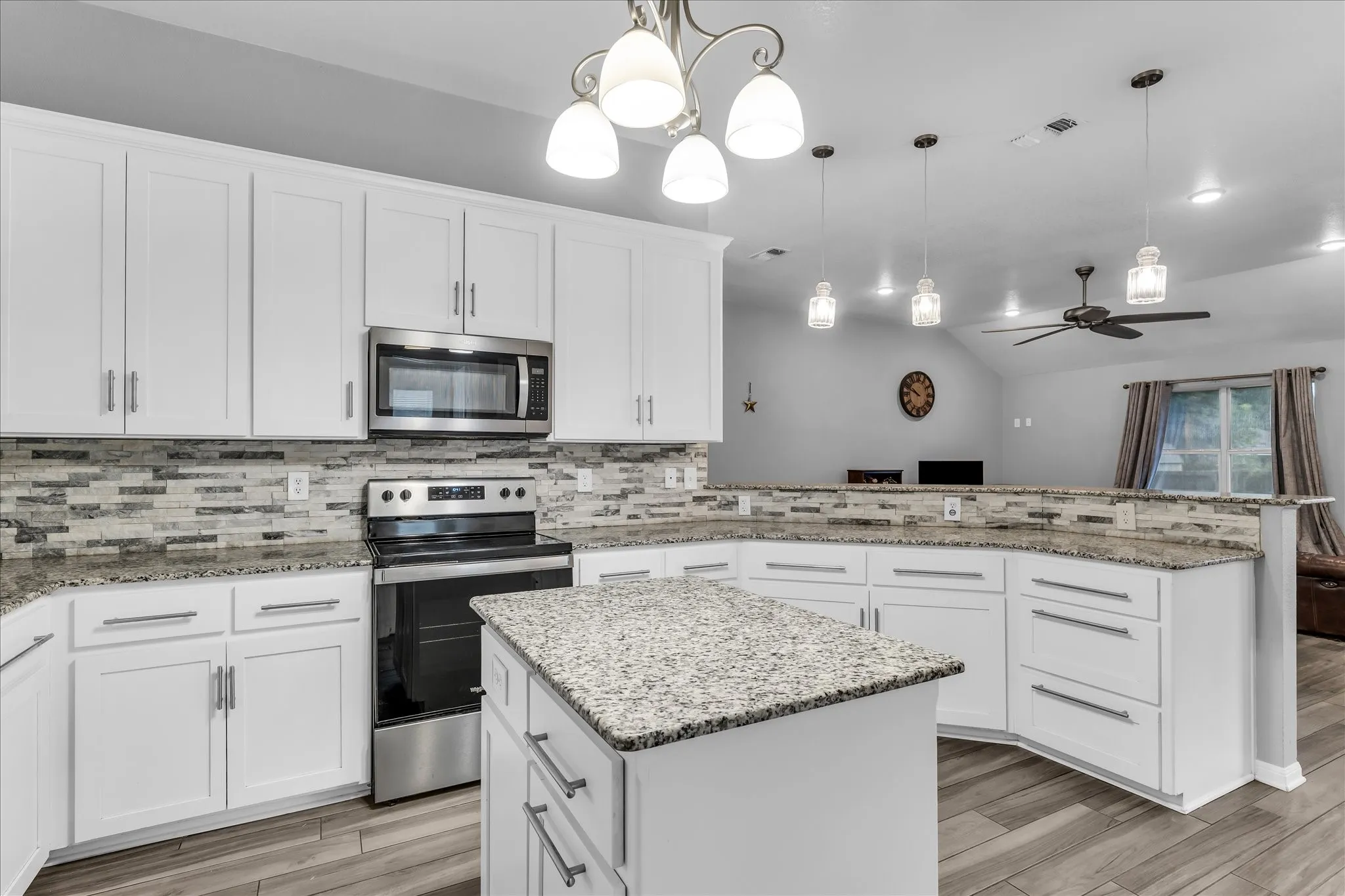 Modern kitchen featuring white cabinetry, granite countertops, a textured tile backsplash, stainless steel appliances, and a central island