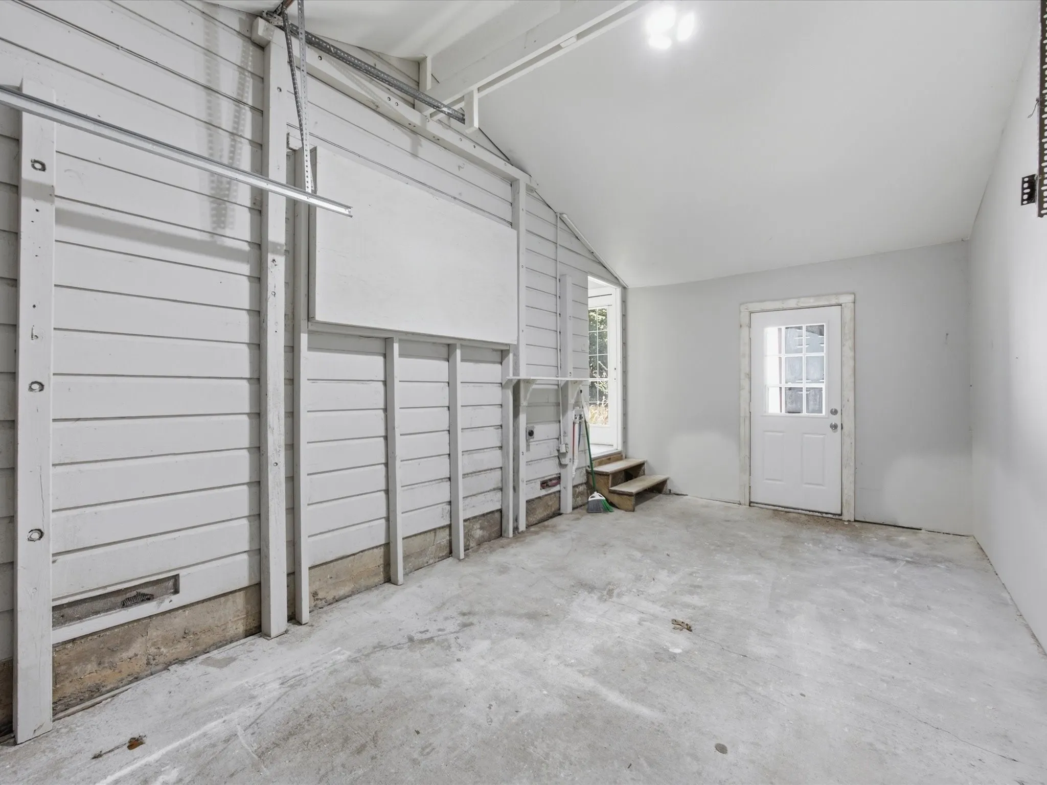 Spacious garage featuring concrete flooring, painted plank walls, a pedestrian entry door with divided lites, and a bright overhead light fixture