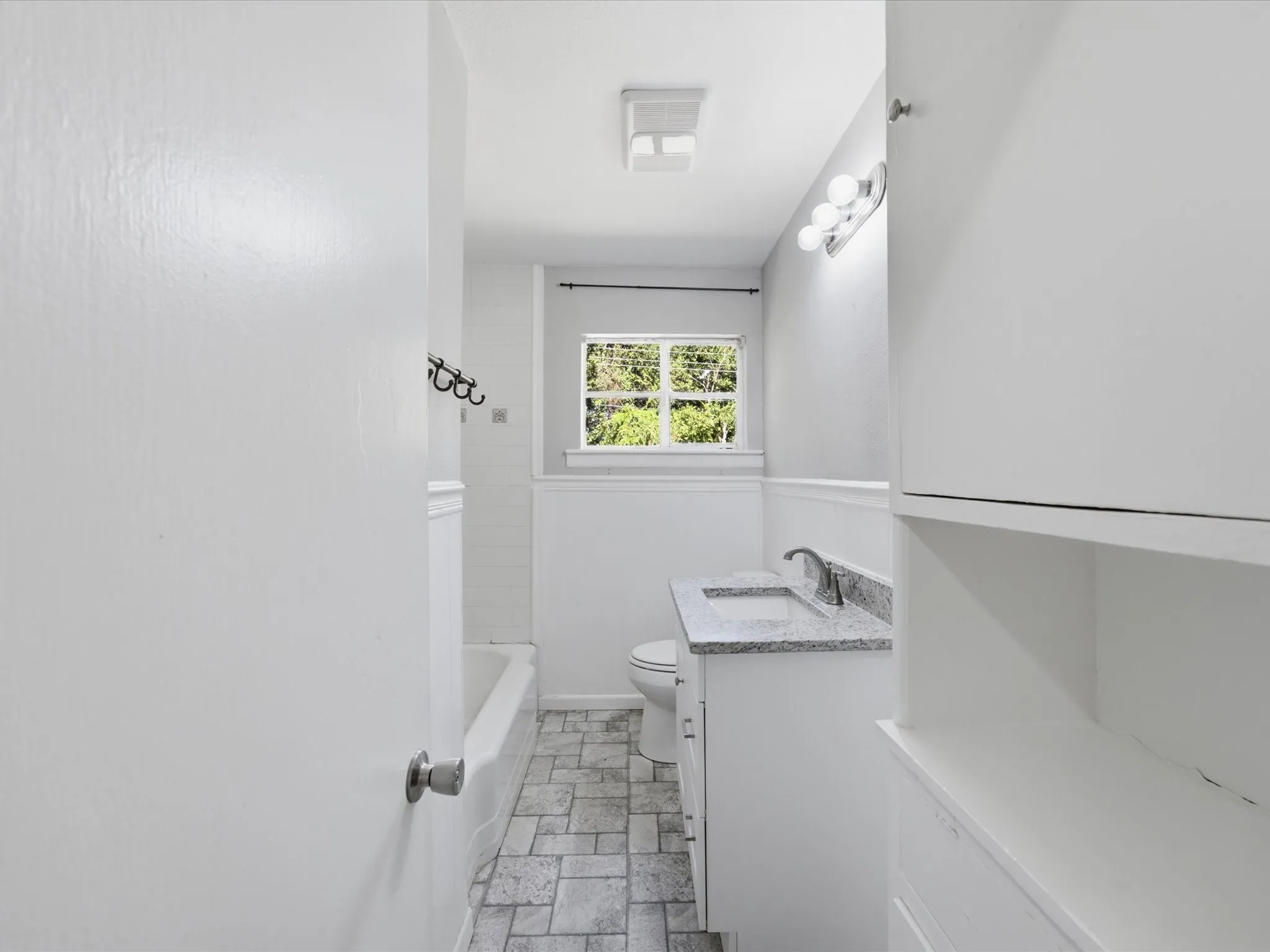 Bathroom featuring a single window, a white vanity with an undermount sink and granite-finish countertop, tiled flooring, a bathtub with subway tile surround, and a ceiling-mounted light fixture