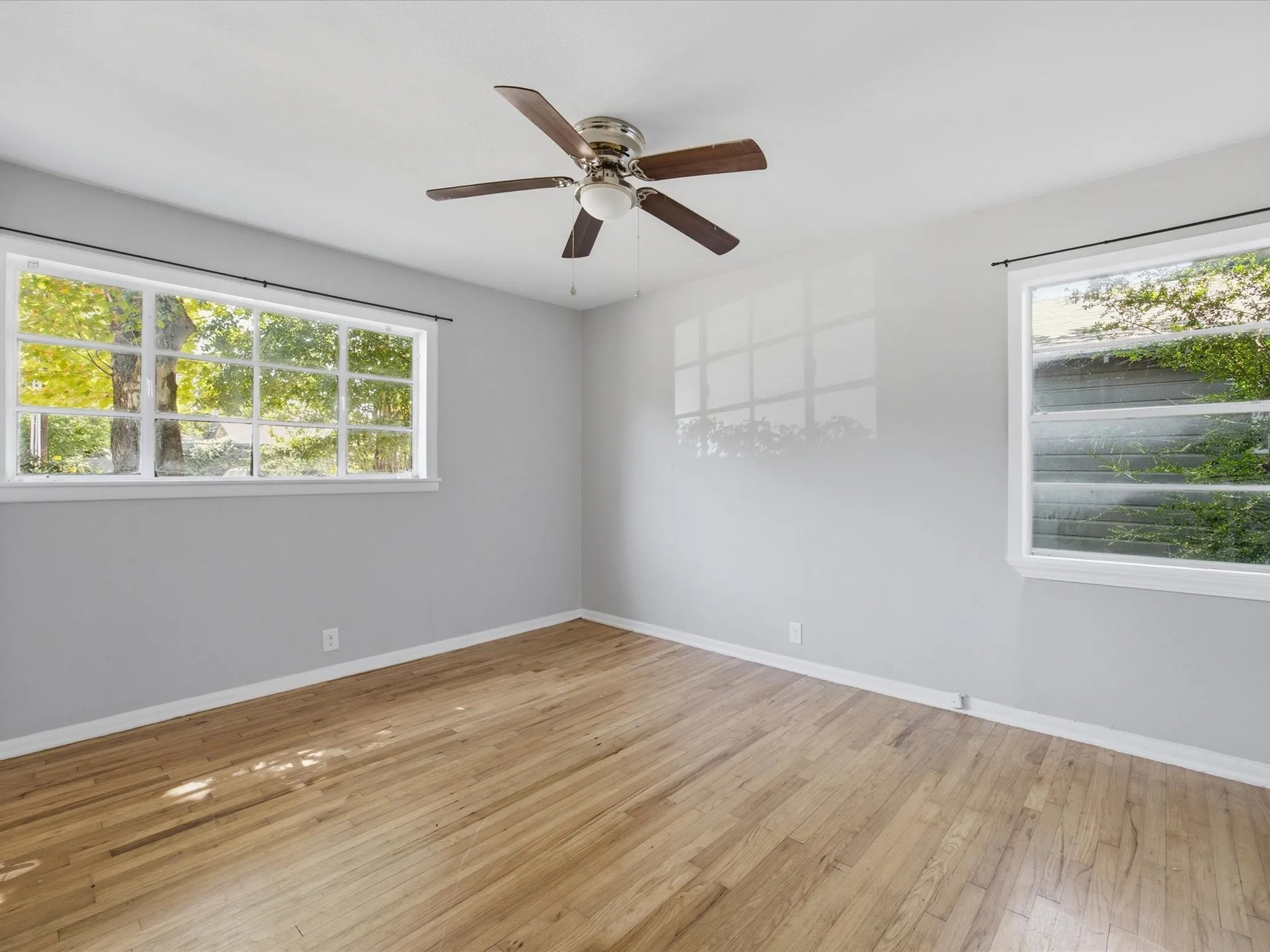 Bright bedroom featuring wood-finish flooring and a ceiling fan with integrated lighting