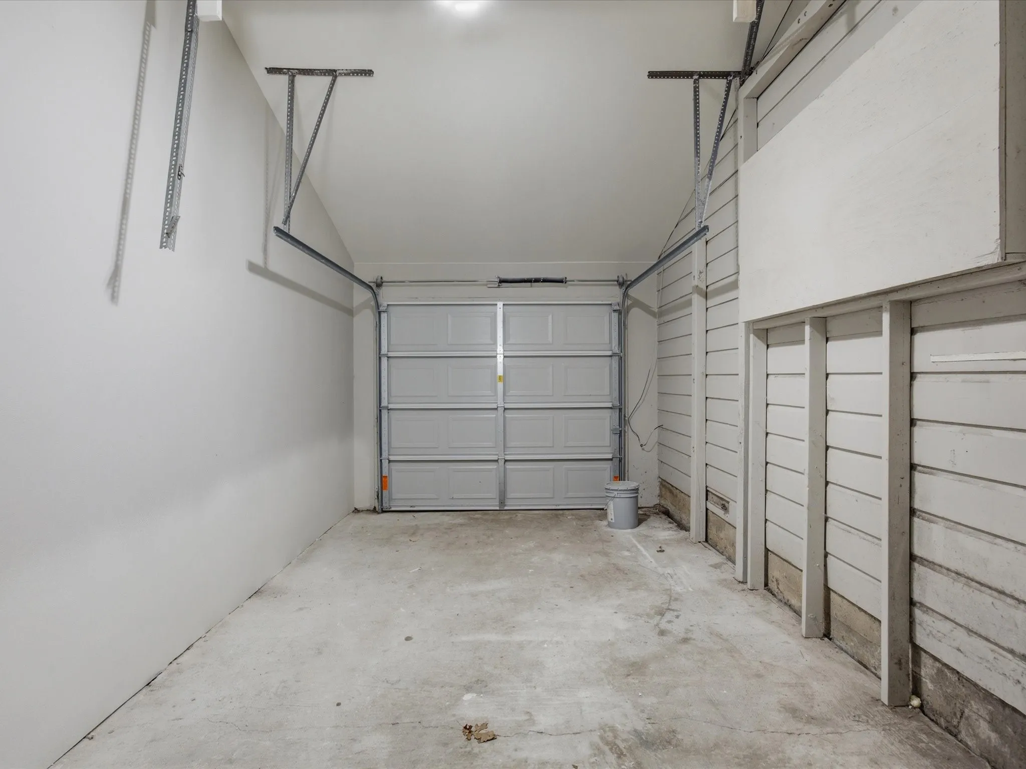Single-car garage featuring a sectional overhead door, concrete flooring, and exposed wall framing