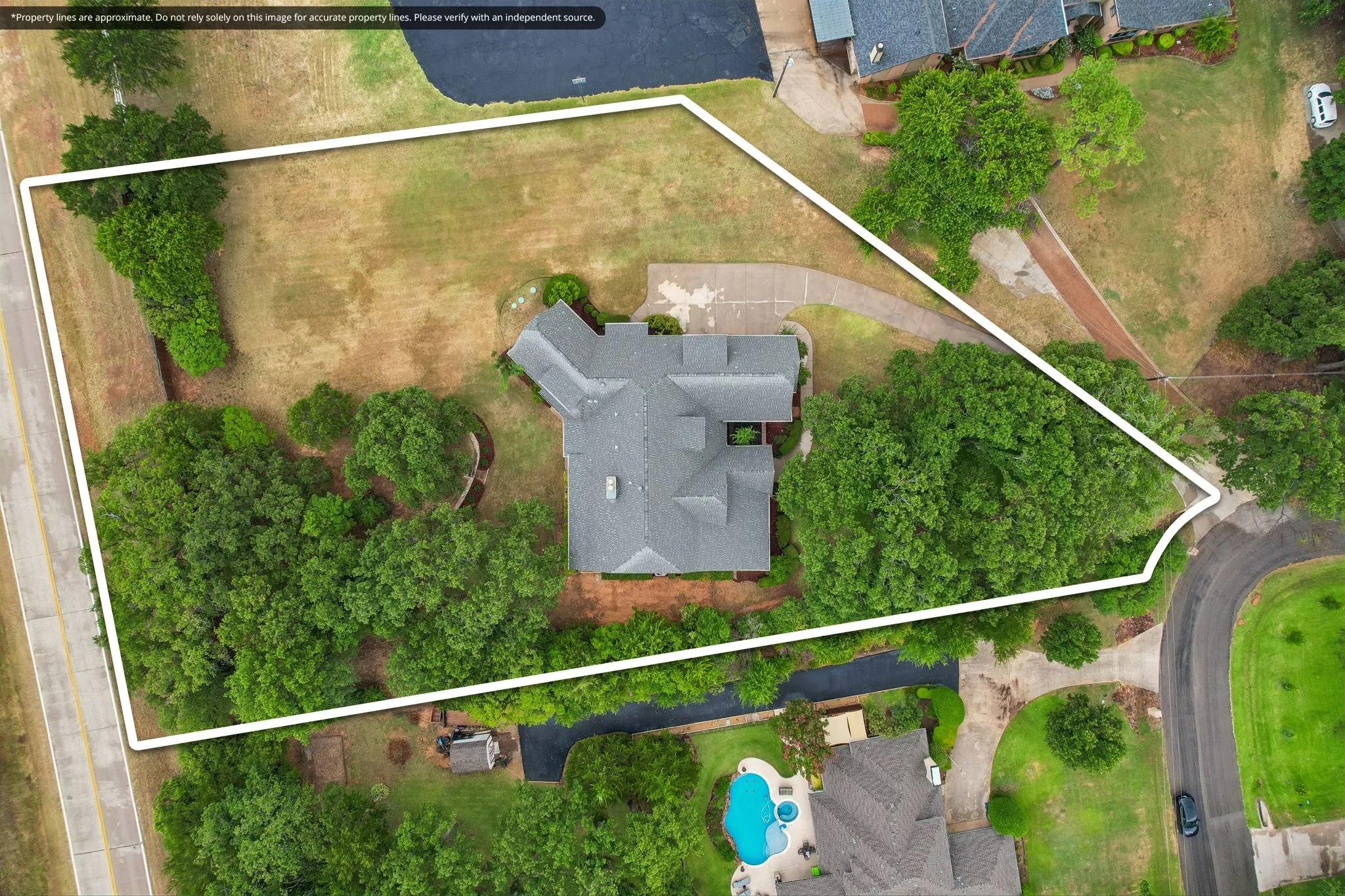 Expansive lot featuring a main residence with a gray shingled roof, mature trees, and a paved driveway