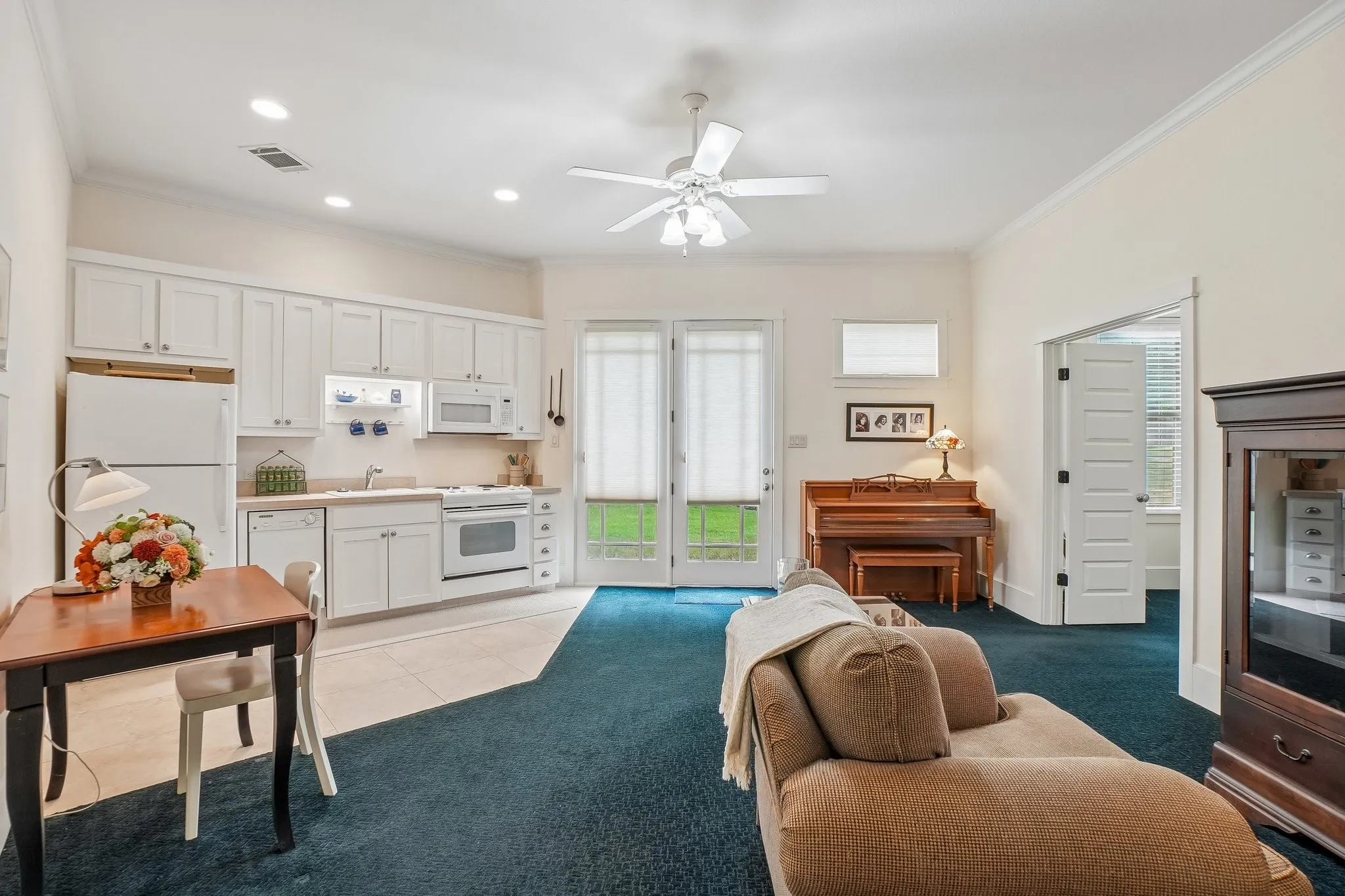 Bright living area featuring a full kitchen with white cabinetry and appliances, a ceiling fan, and double French doors opening to outdoor space