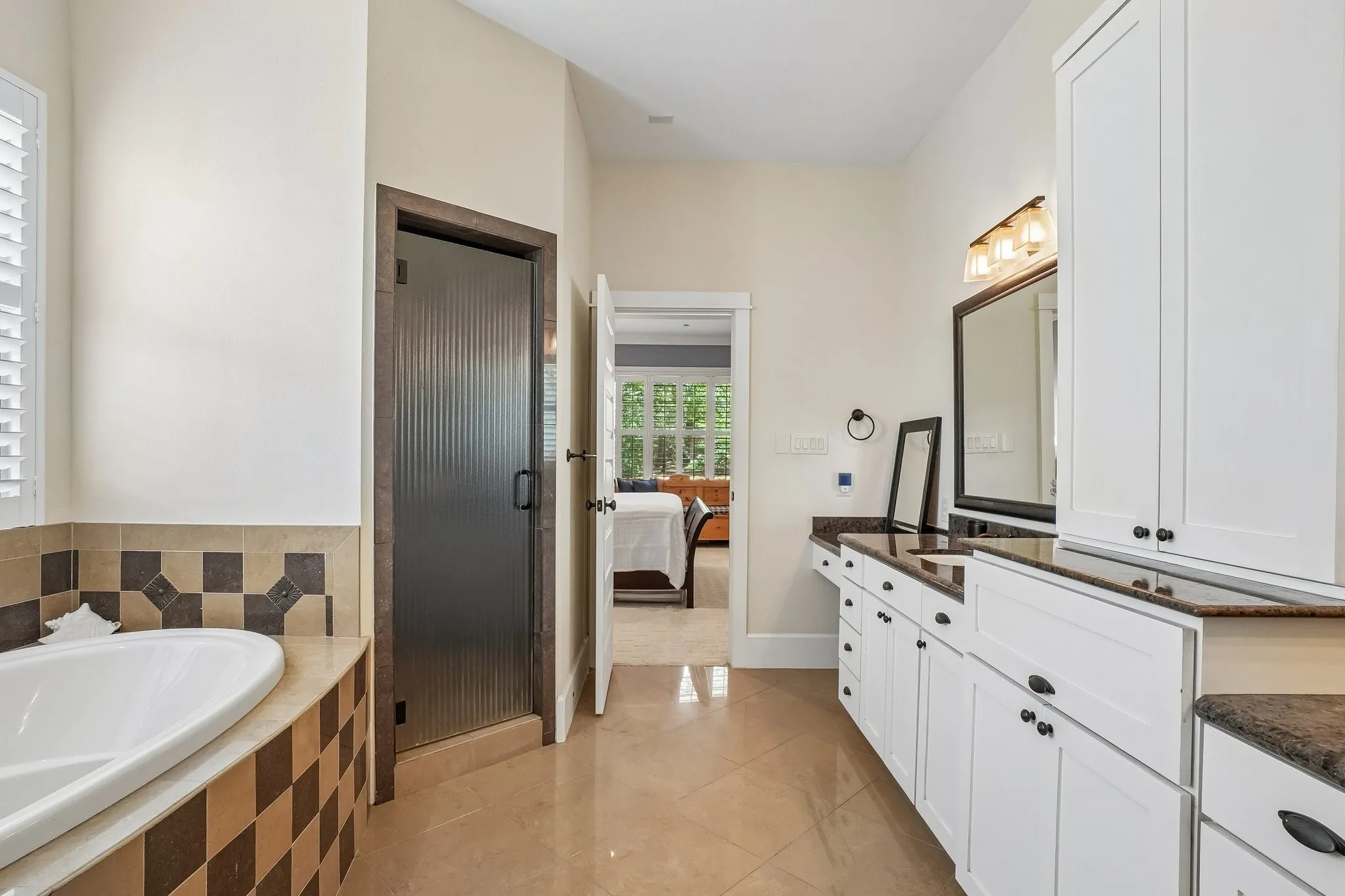 Bathroom featuring a standalone soaking tub with decorative tile surround, a fluted glass shower enclosure, a dual vanity with white cabinetry and dark countertops, and tile flooring