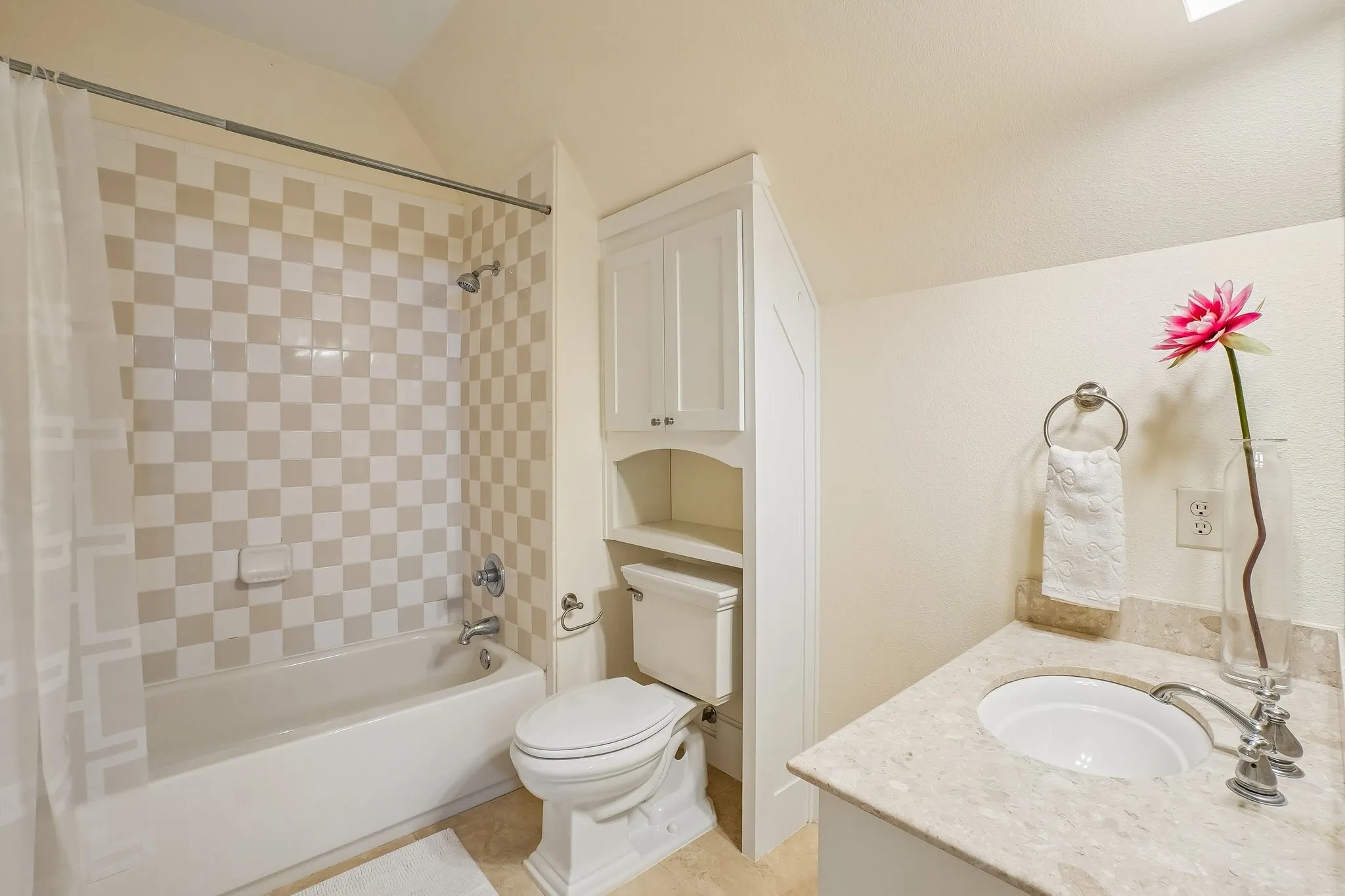 Bathroom featuring a built-in tub with a checkerboard tiled surround, a toilet, a vanity with an integrated sink and light-toned countertop, and white cabinetry