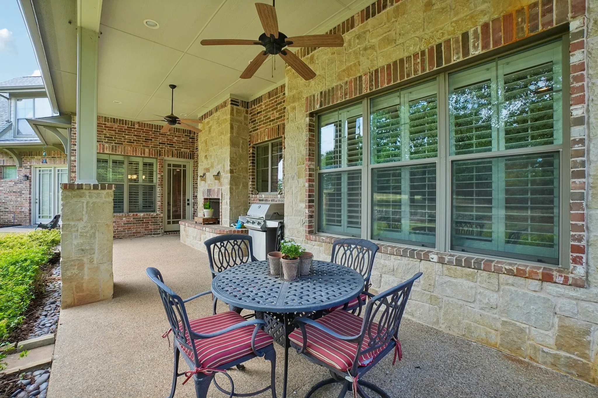 Covered patio featuring an exposed aggregate concrete surface, brick and stone exterior, two ceiling fans, and a built-in outdoor fireplace