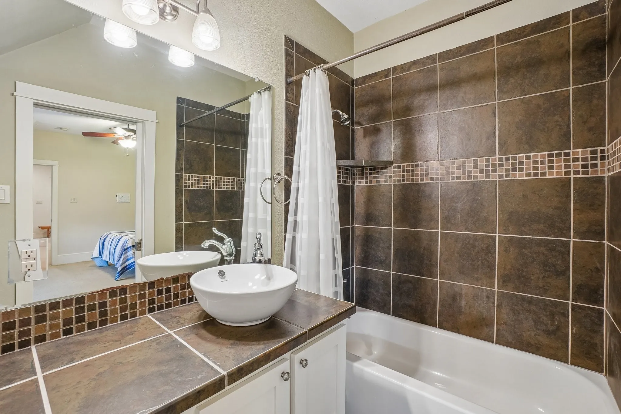 Bathroom featuring a ceramic vessel sink, tile countertop, white cabinetry, and a full tile bath surround with an accent mosaic border