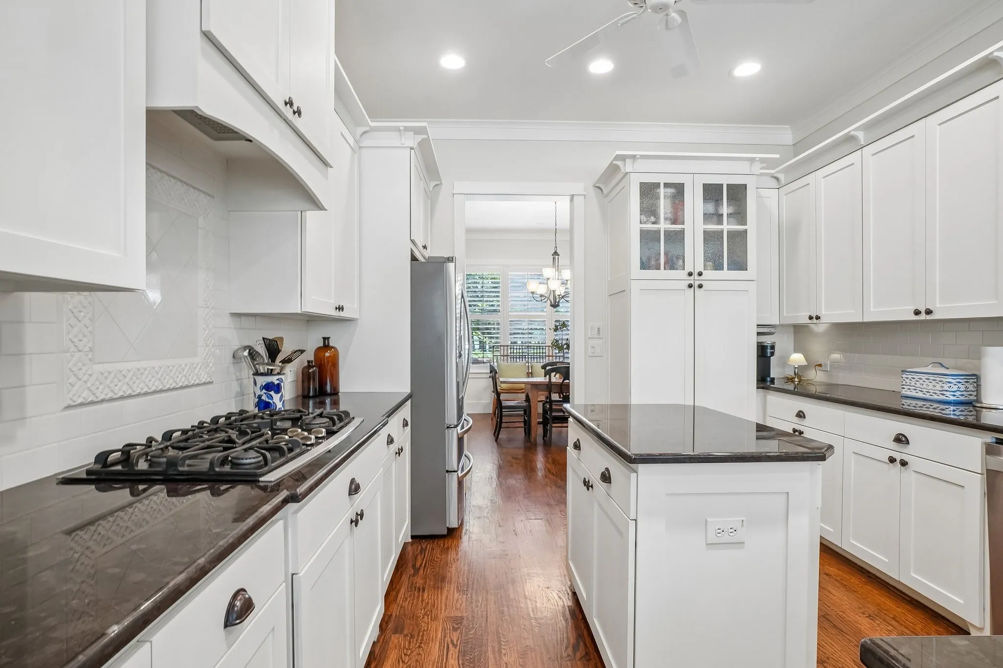 Bright kitchen featuring white shaker cabinetry, dark countertops, a built-in gas range, stainless steel appliances, and wood-finish flooring