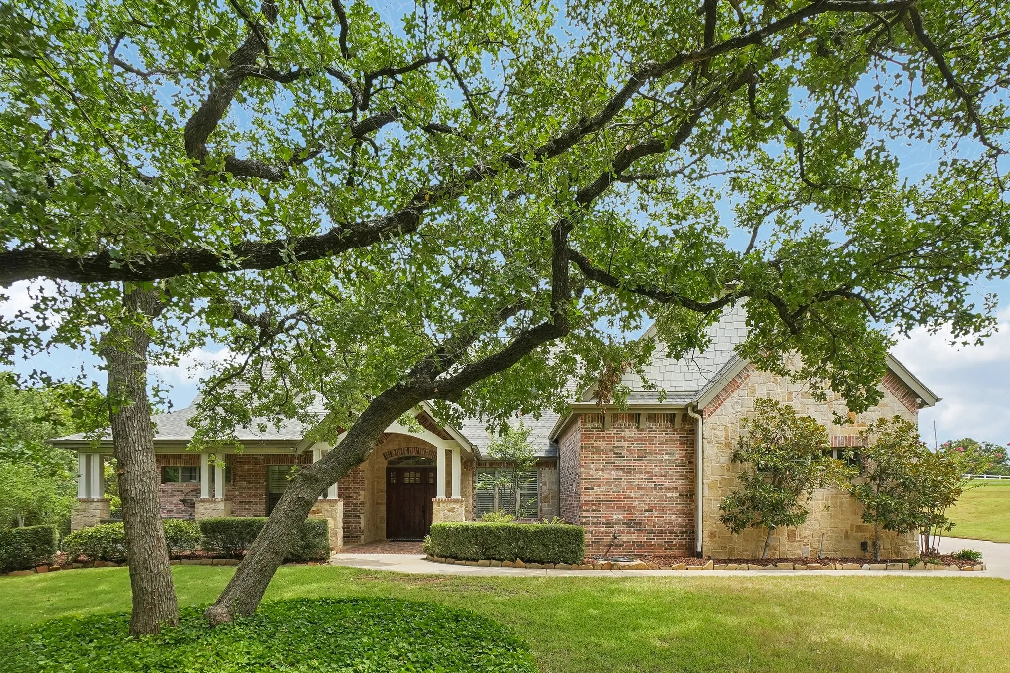 Stone and brick exterior with a prominent arched entry, surrounded by mature trees and manicured landscaping