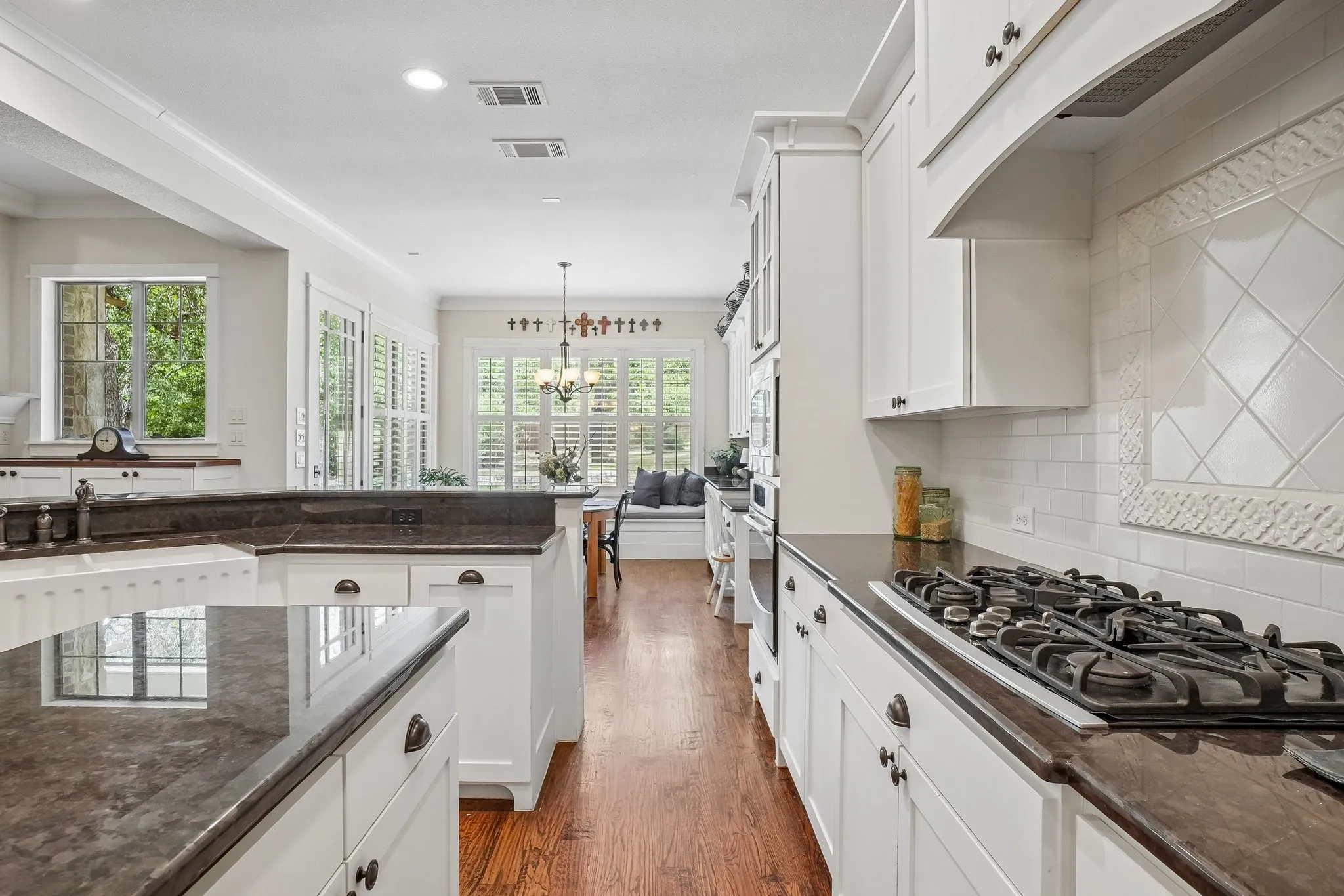Kitchen featuring white cabinetry, dark stone countertops, a gas range with an overhead vent hood, a decorative tile backsplash, and wood-finish flooring