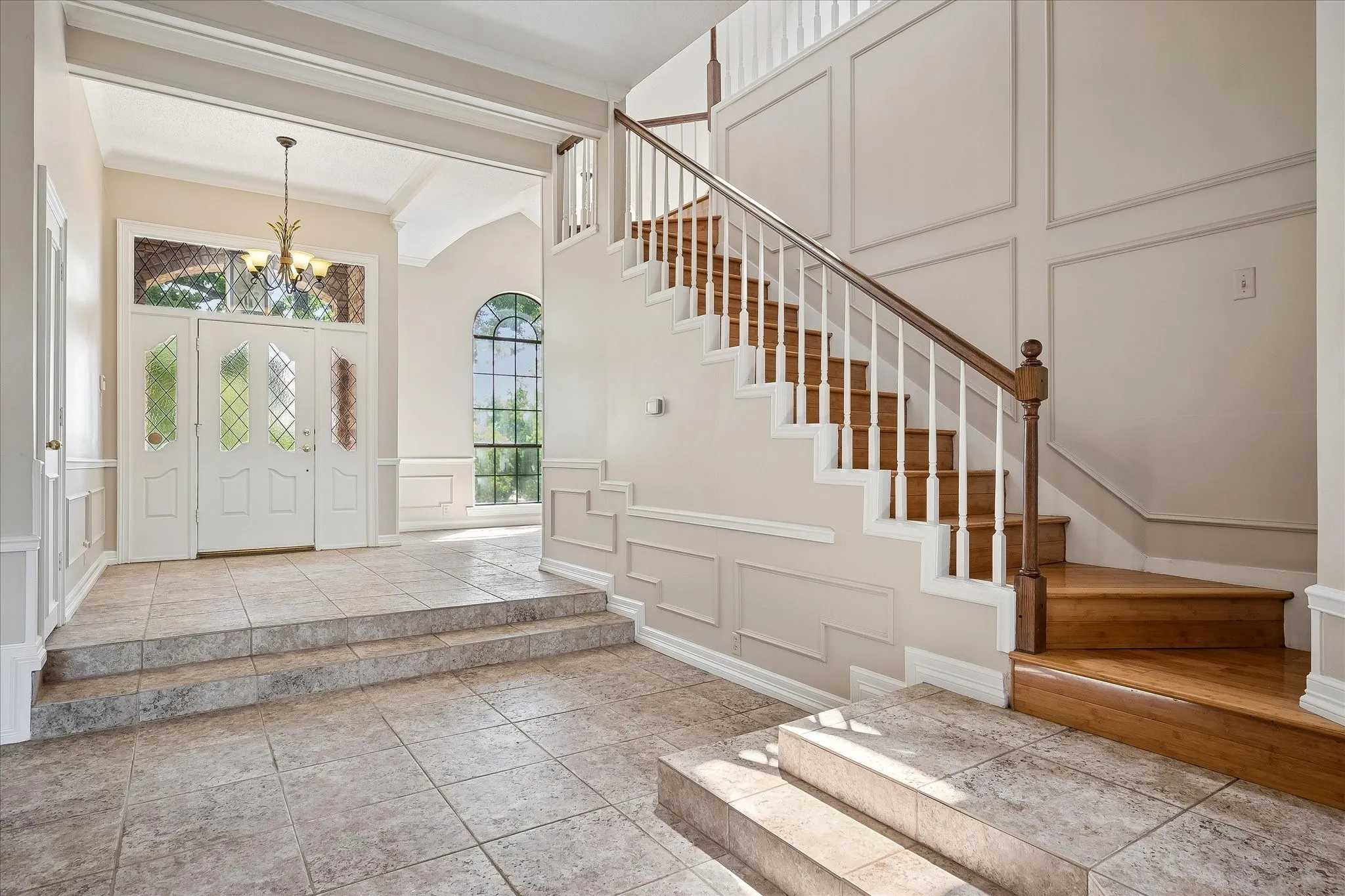 Foyer featuring a grand staircase with wood treads and white balusters, decorative wall paneling, and a double entry door with leaded glass panels