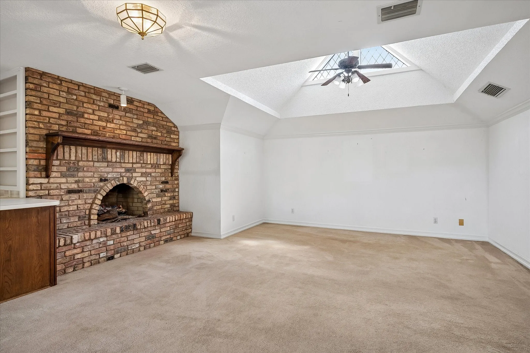 Spacious room featuring a brick fireplace with a wood mantle, an arched firebox, and built-in shelving
