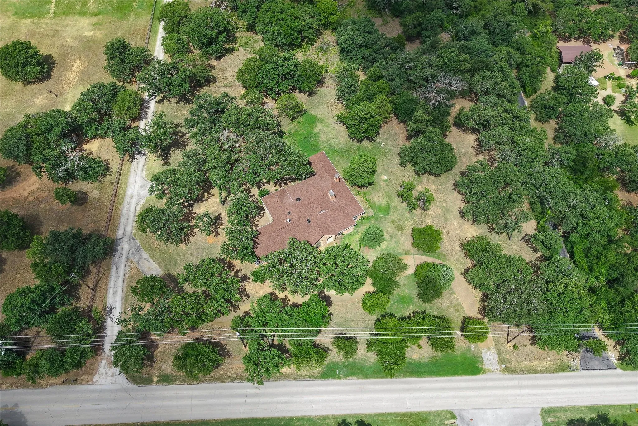 Private residential property with a reddish-brown shingled roof, surrounded by numerous mature trees and a gravel driveway