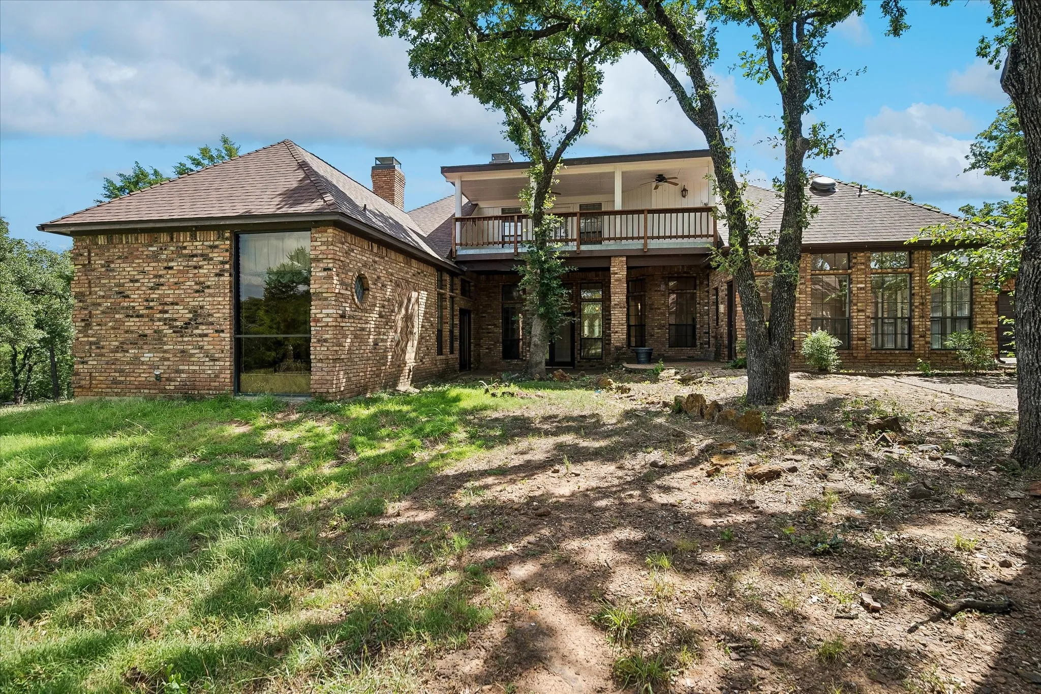 Brick exterior featuring a two-story design with a second-level balcony, a ground-level covered patio, expansive windows, and a circular window detail