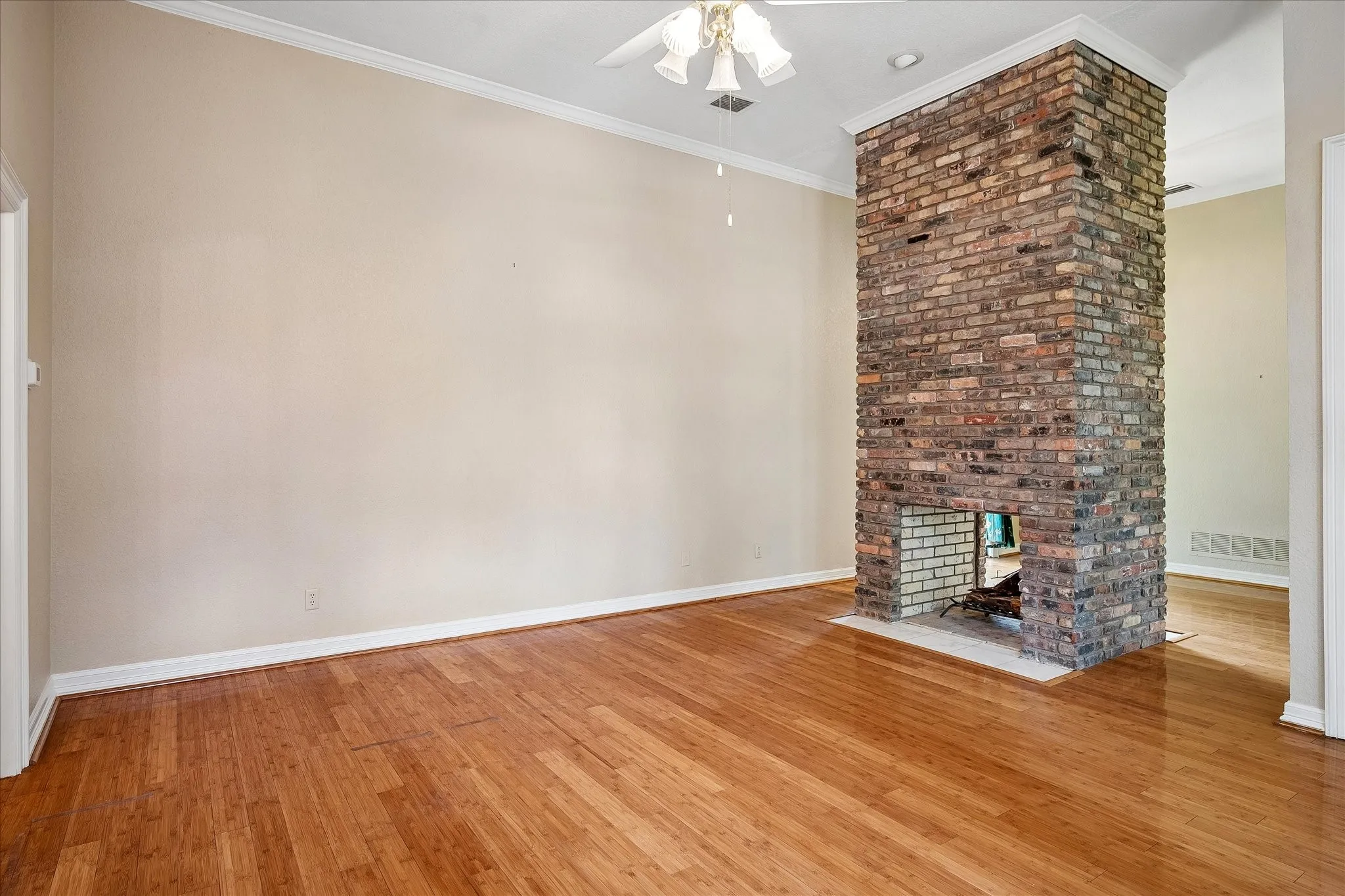 Spacious room featuring a prominent brick fireplace with a white hearth, light-toned walls, and wood-finish flooring