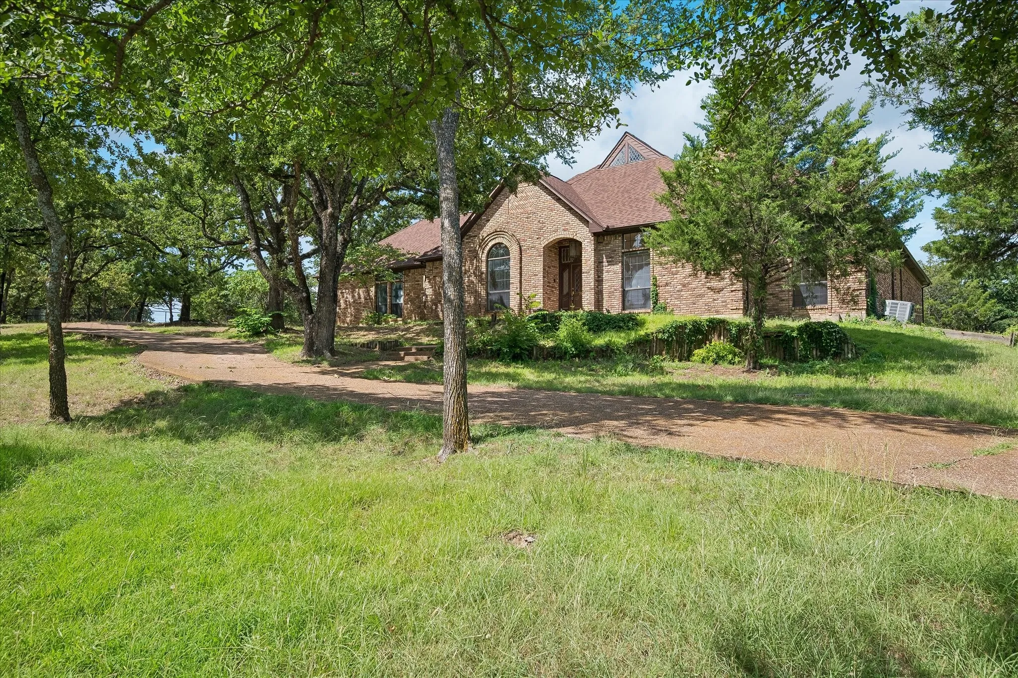 Brick exterior residence featuring a gabled roofline, arched entry, and mature landscaping