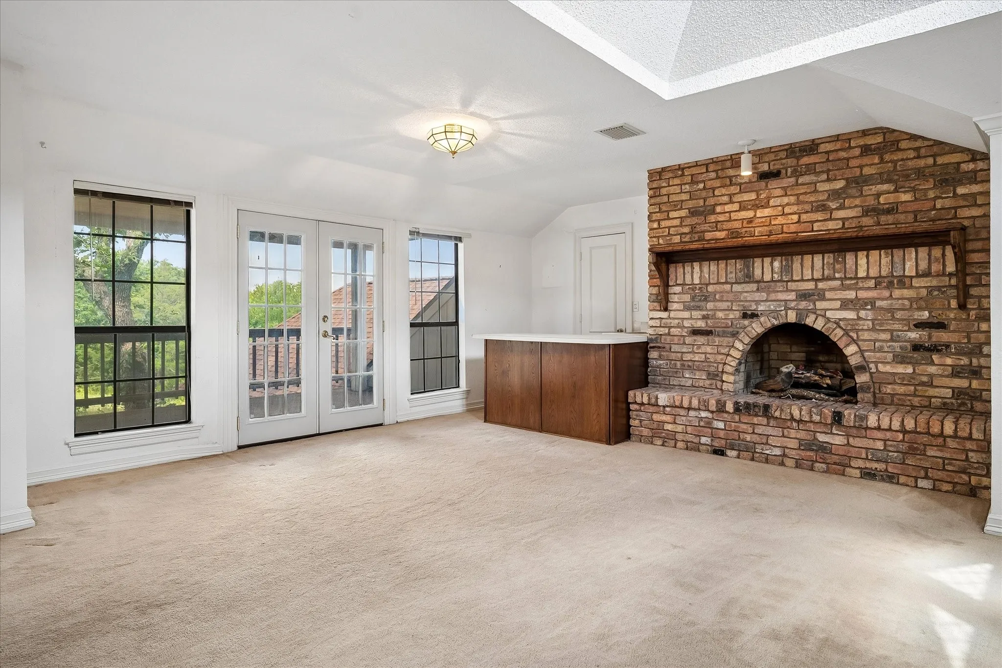 Spacious room featuring a prominent brick fireplace with an arched firebox and wooden mantel