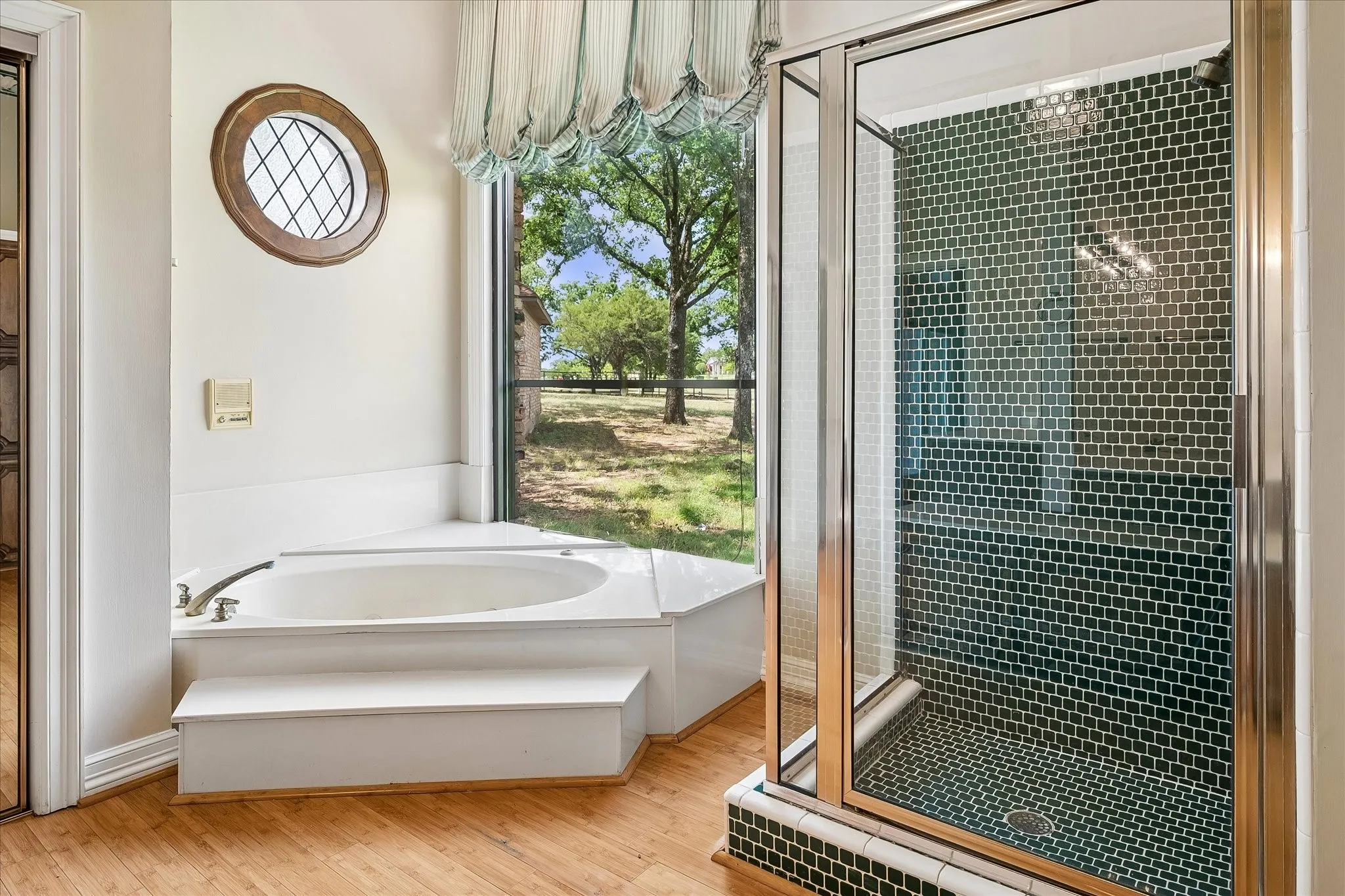 Corner soaking tub with integrated steps, accompanied by a separate glass-enclosed shower featuring dark green mosaic tile