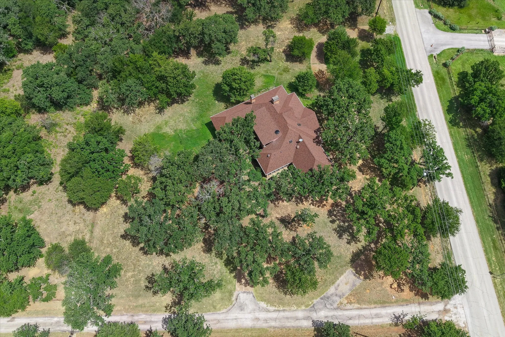 Expansive property with a multi-gabled brown shingle roof, surrounded by mature deciduous trees