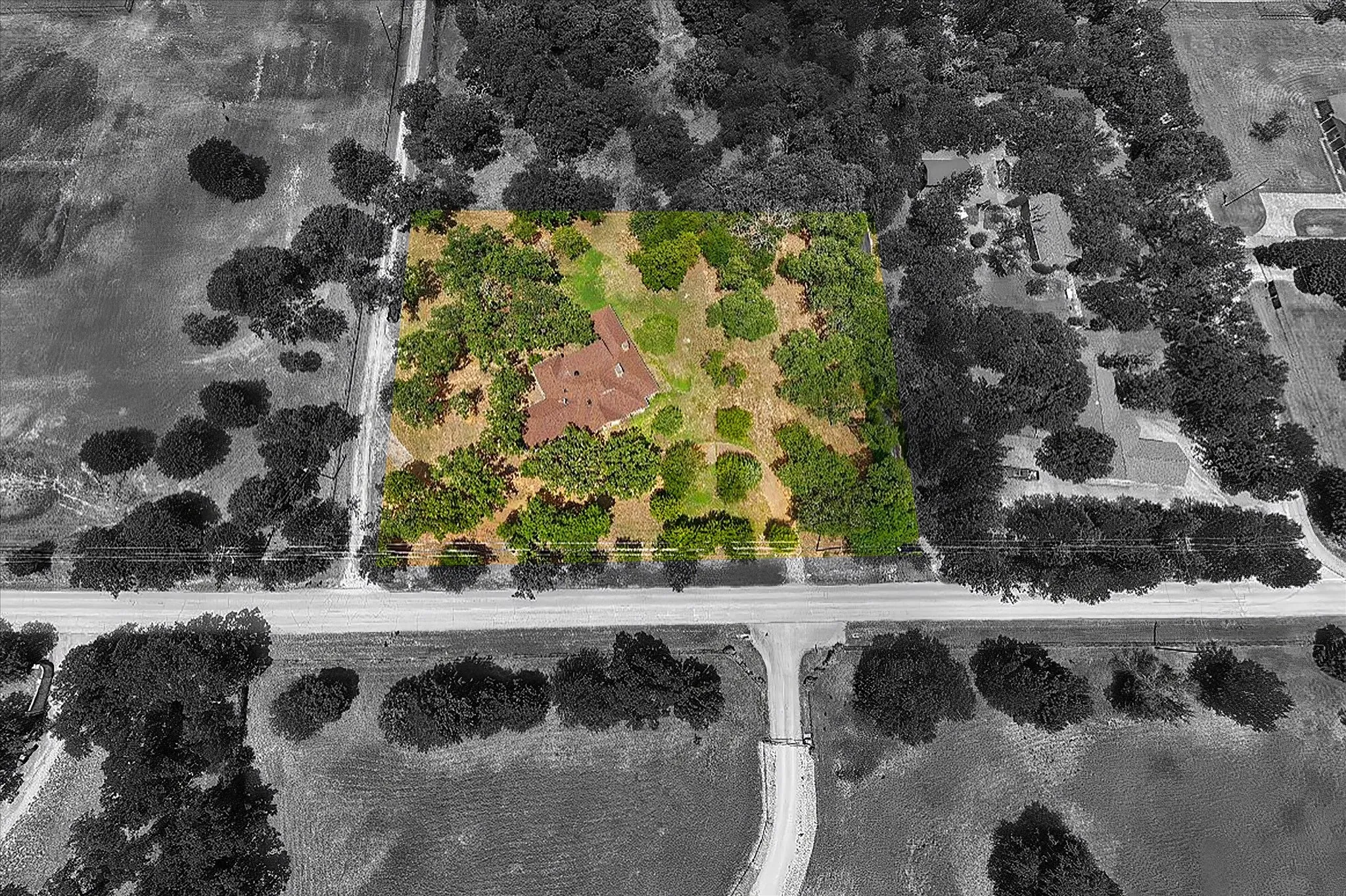 Expansive property featuring a single-story residence with a red tile roof, set amidst mature trees and open land