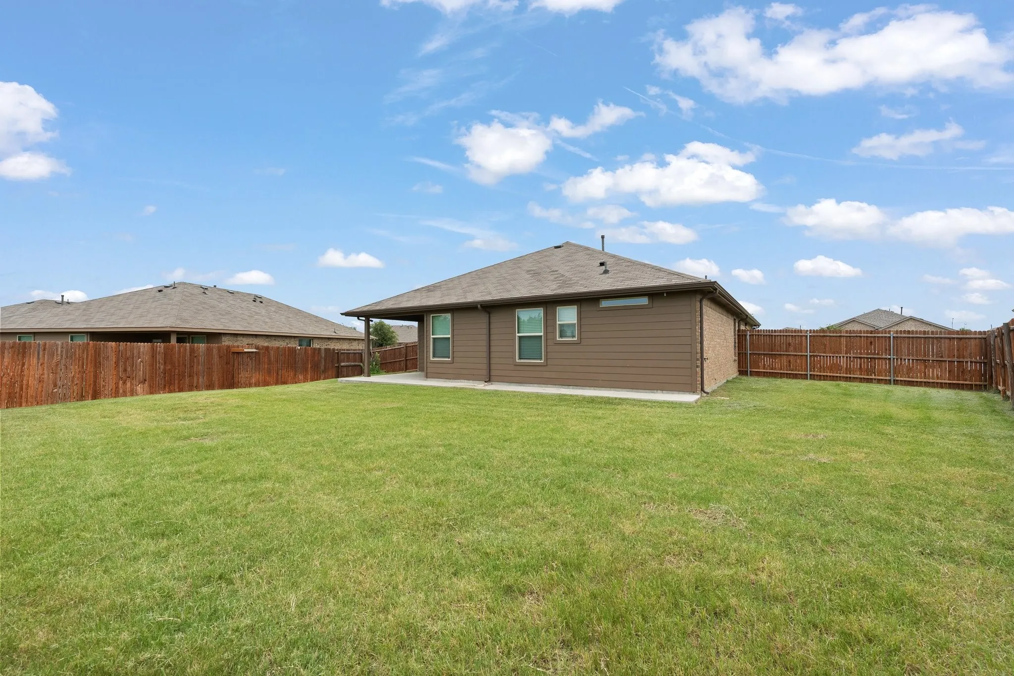 Expansive backyard featuring a lush lawn, privacy fencing, a covered patio, and a blend of brick and siding exterior finishes
