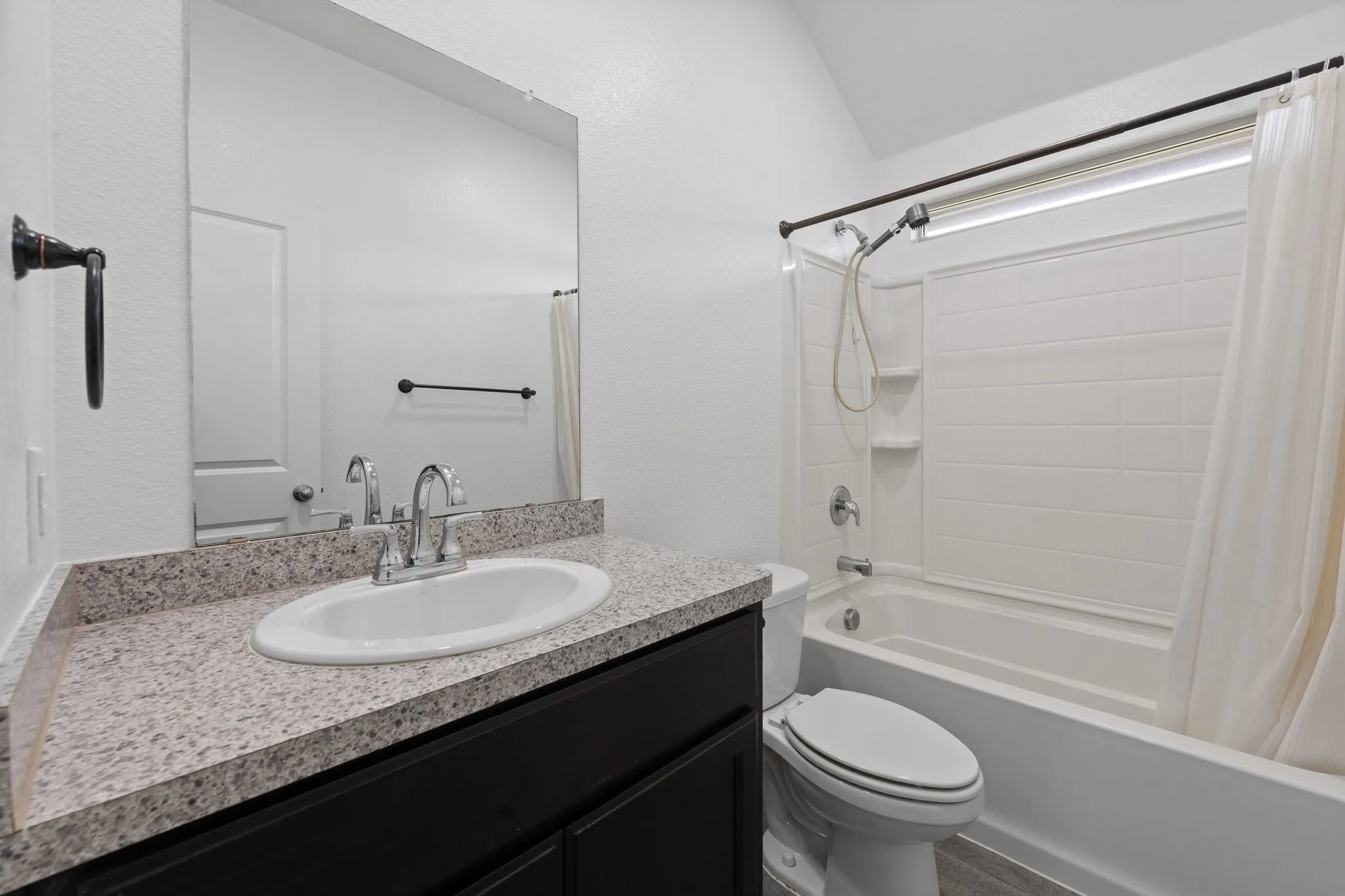 Bathroom featuring a dark wood-finish vanity with a speckled countertop, an undermount sink, and a large wall-mounted mirror