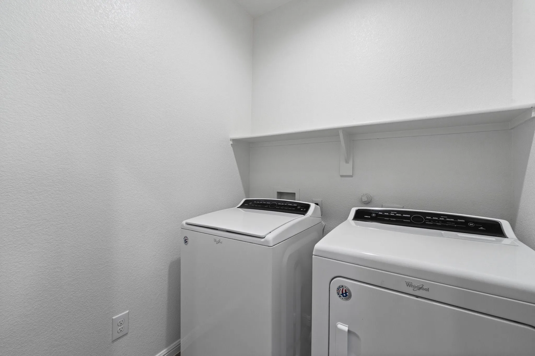 Dedicated laundry space featuring a white wall shelf, textured walls, and a white appliance set
