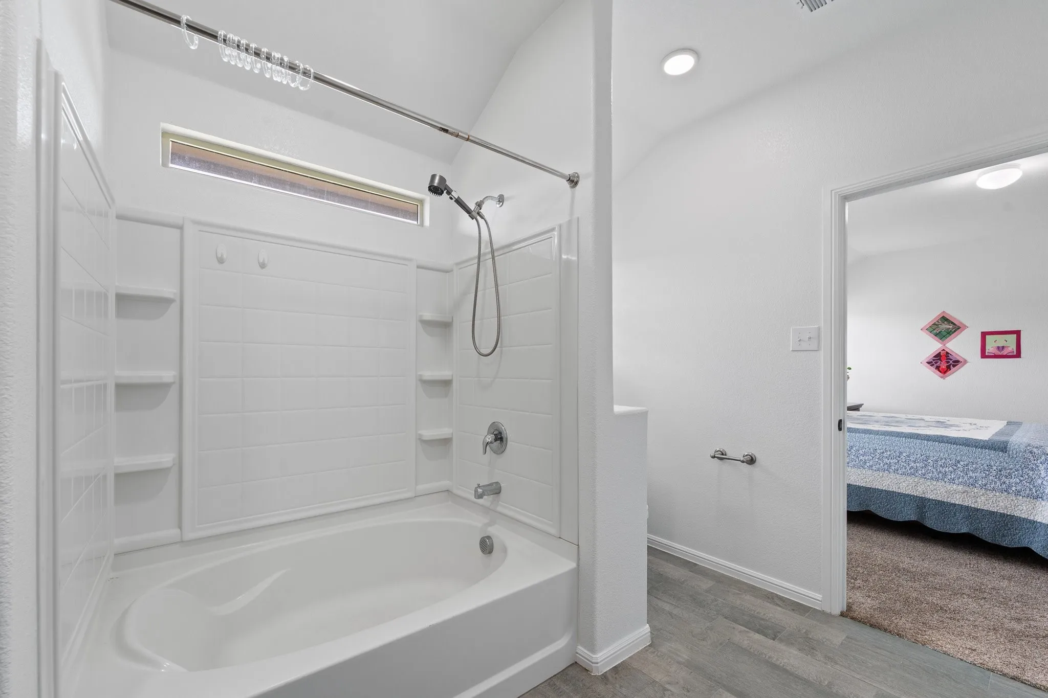 Bathroom featuring a white tub-shower combination with integrated shelving, a chrome showerhead with a handheld sprayer, and a transom window