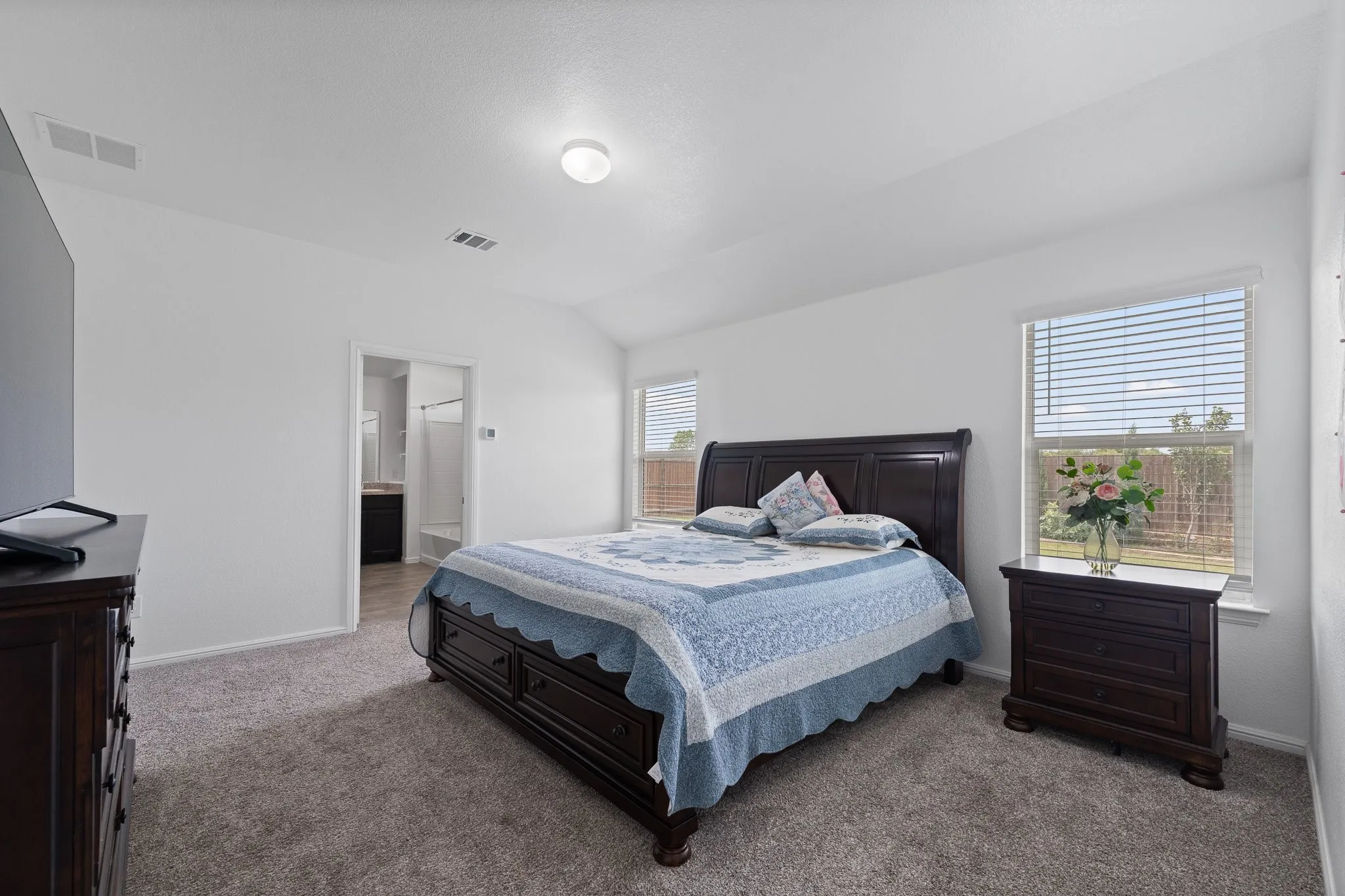 Carpeted room featuring white walls, a vaulted ceiling, and two windows with horizontal blinds