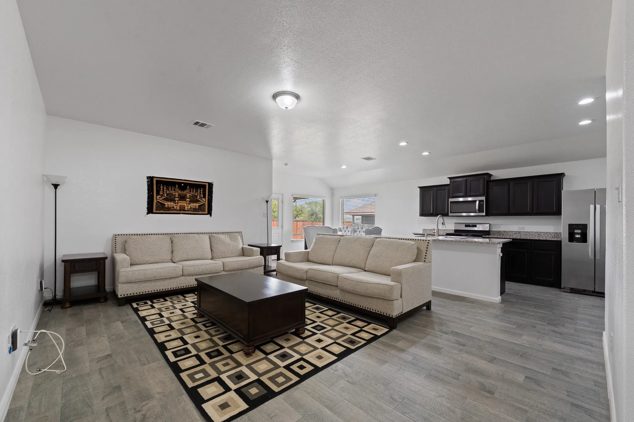 Open-concept living area featuring wood-finish flooring, recessed lighting, and a kitchen with dark cabinetry, stainless steel appliances, and a breakfast bar with stone countertops