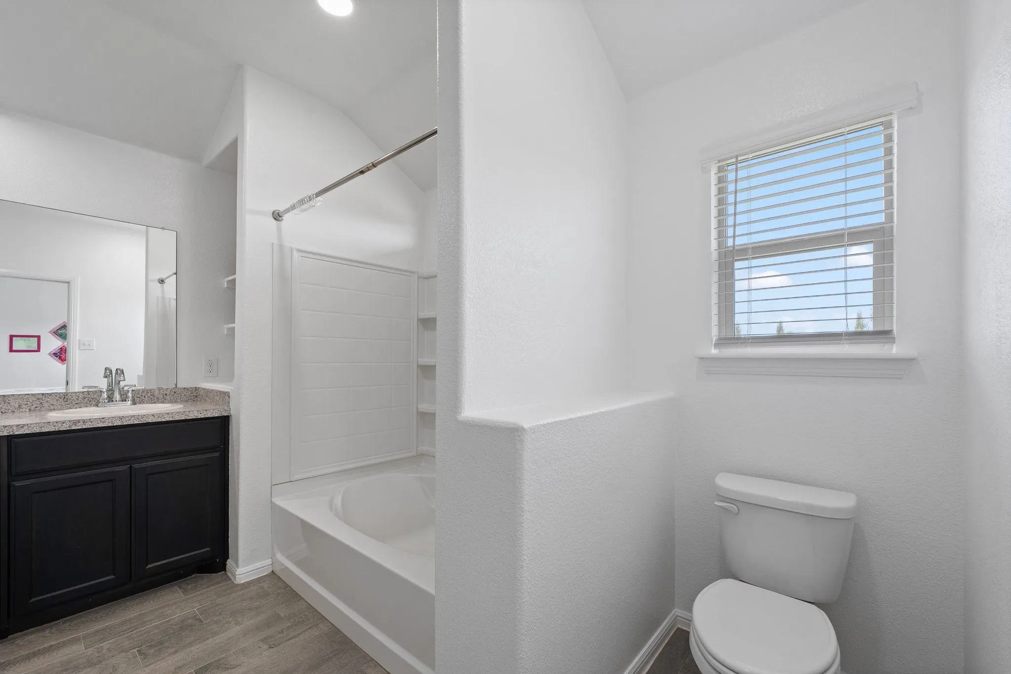 Bathroom featuring a combination shower and tub, wood-finish flooring, dark wood vanity with a light-colored countertop, and a window with blinds