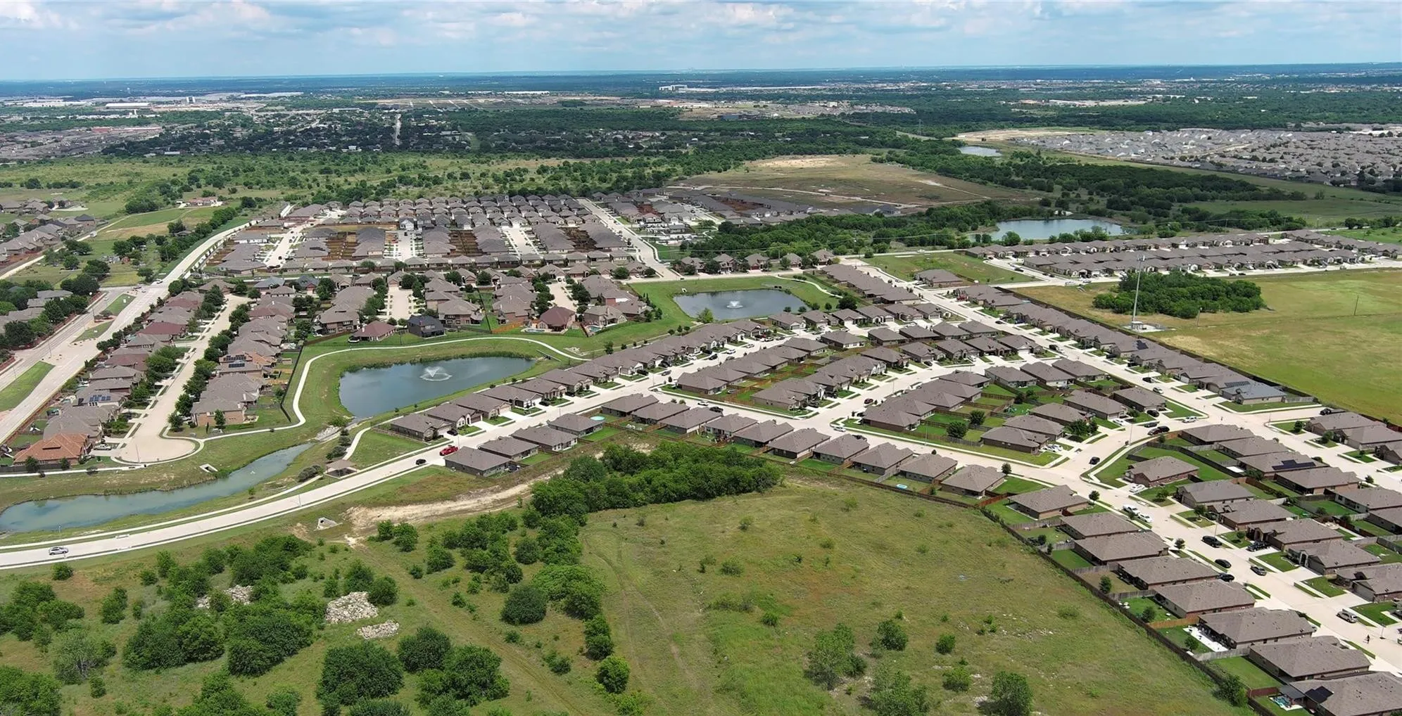 Aerial perspective showcasing a residential community with multiple streets and individual homes, punctuated by two ponds featuring water fountains