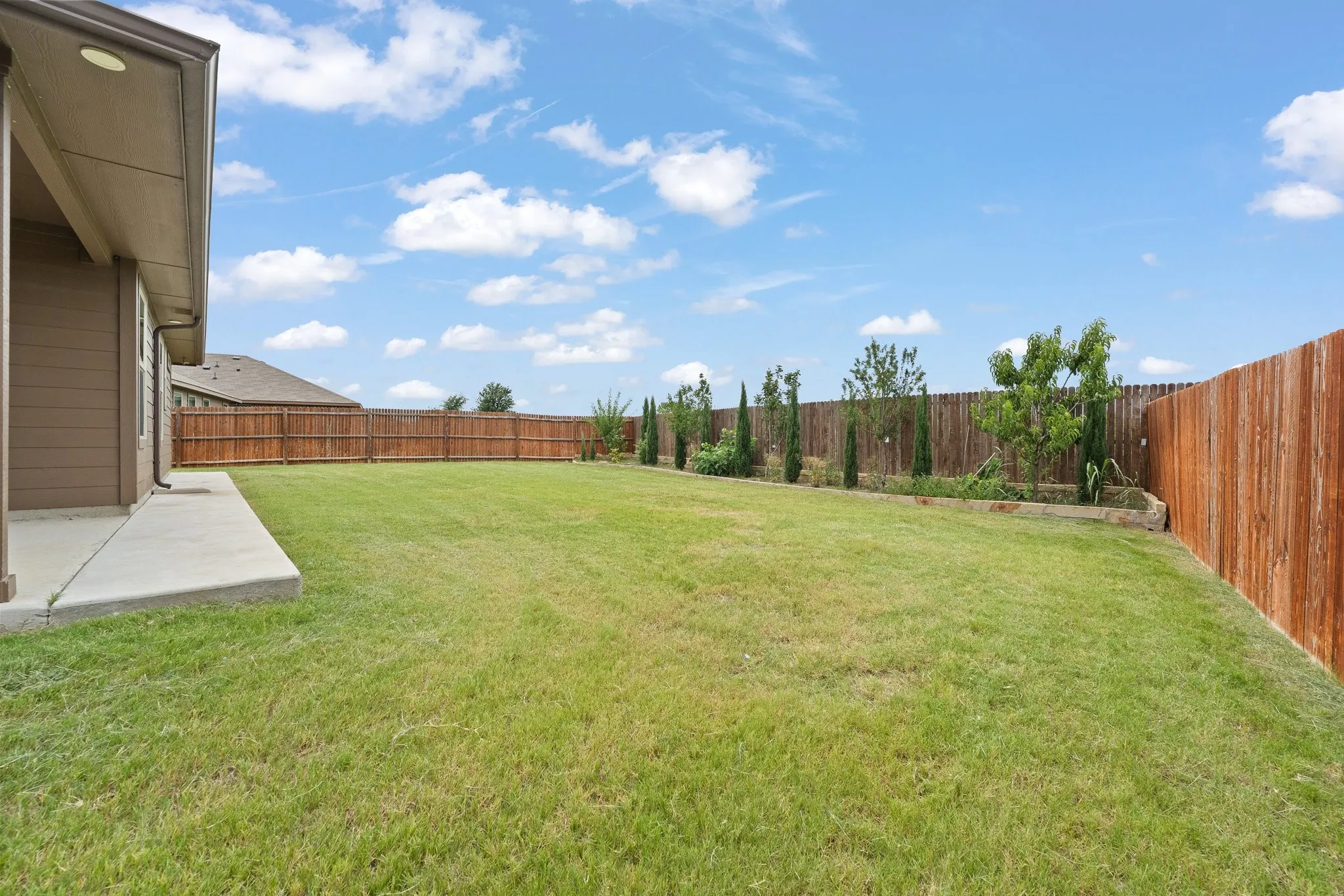 Spacious backyard featuring a large green lawn, a concrete patio, and a wood privacy fence