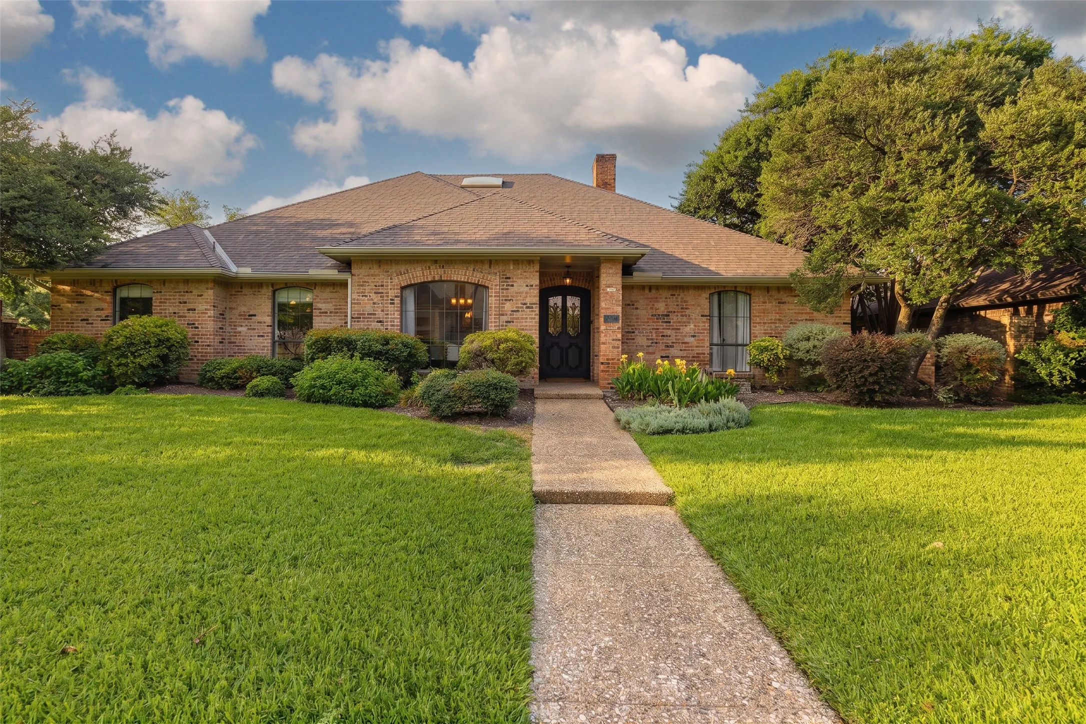 Traditional brick exterior with a dark entry door, arched window, and mature landscaping
