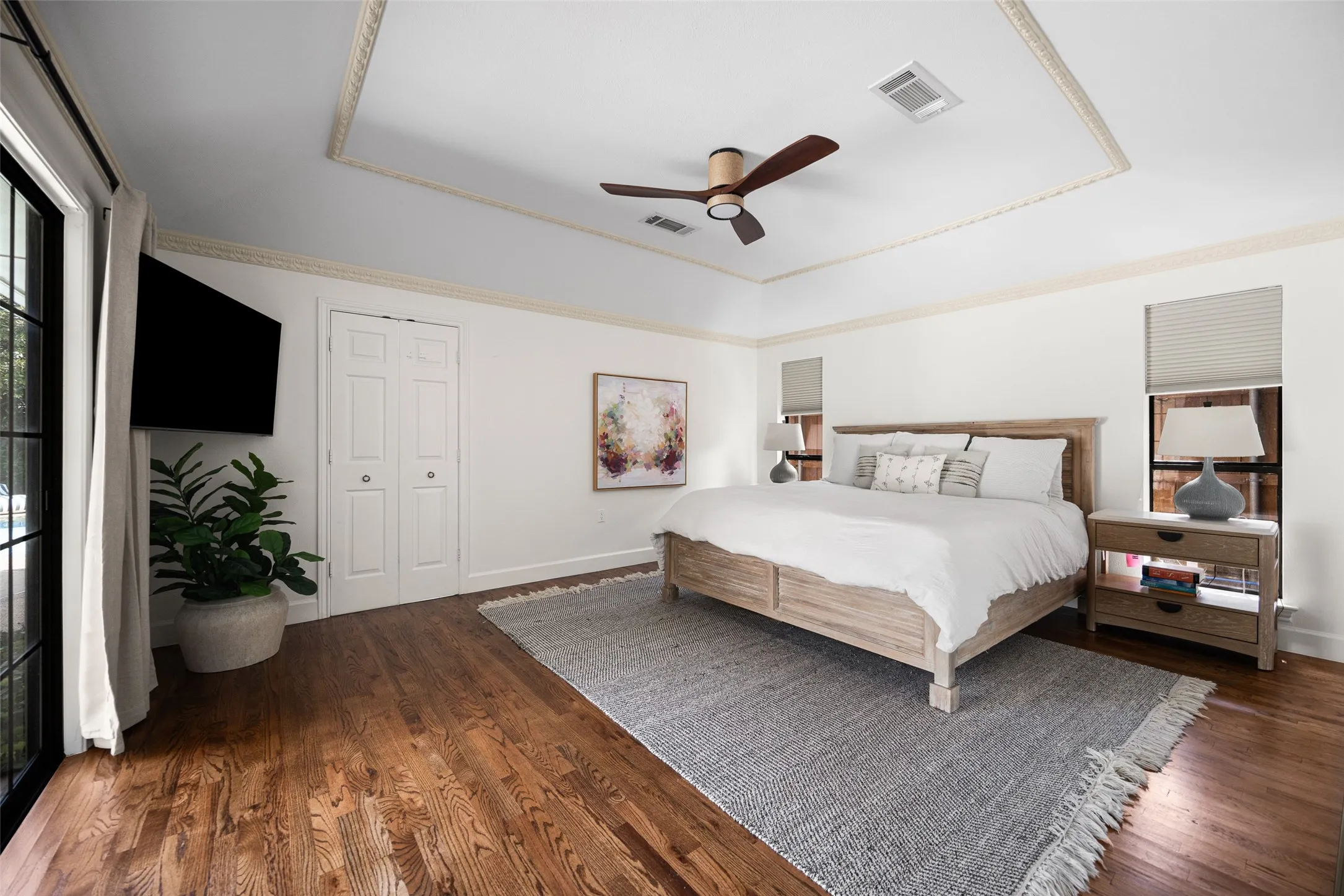 Spacious room featuring wood-finish flooring, a tray ceiling with decorative molding, and a ceiling fan
