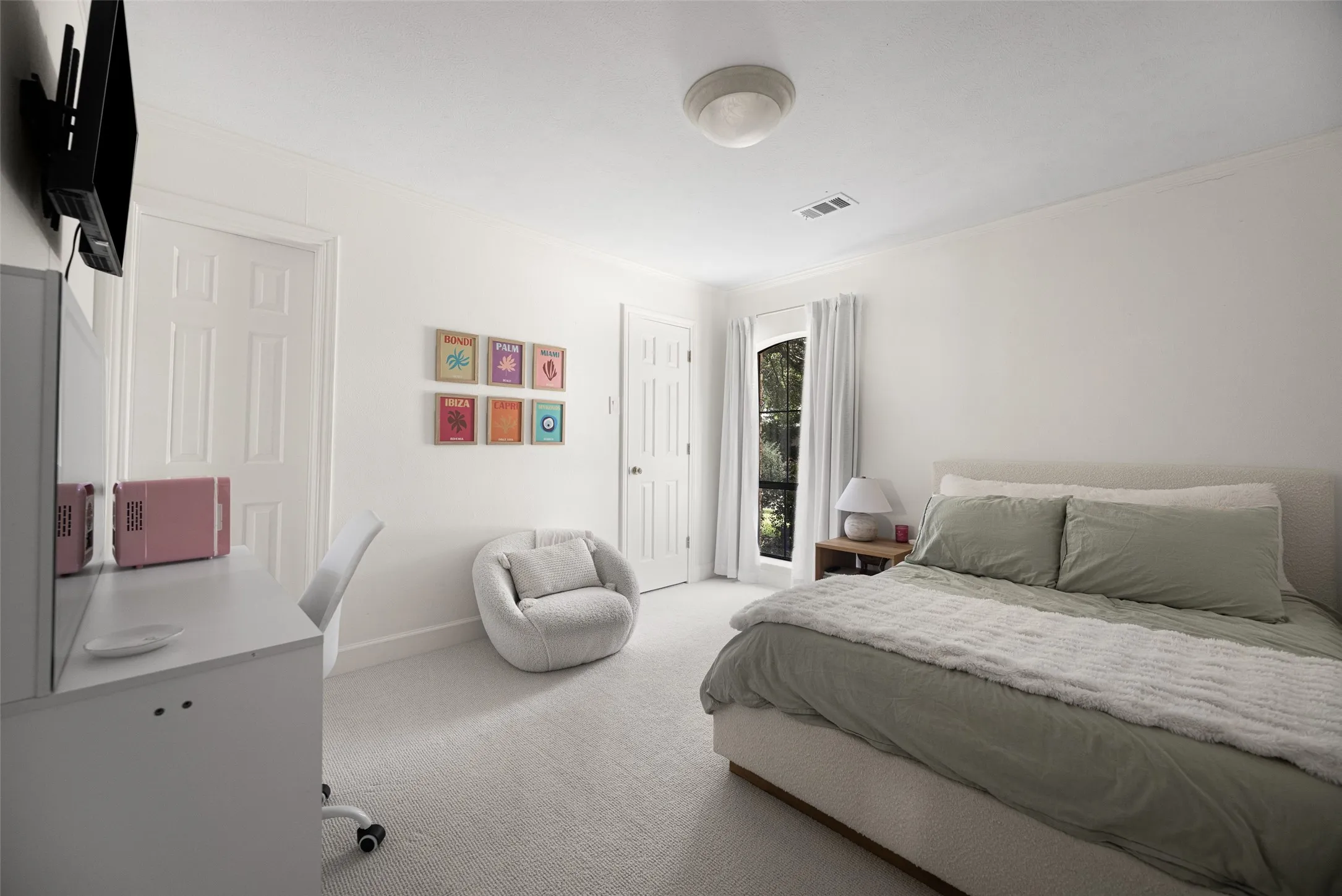 Spacious bedroom featuring light-colored carpeting, white painted walls, and a large window with white curtains