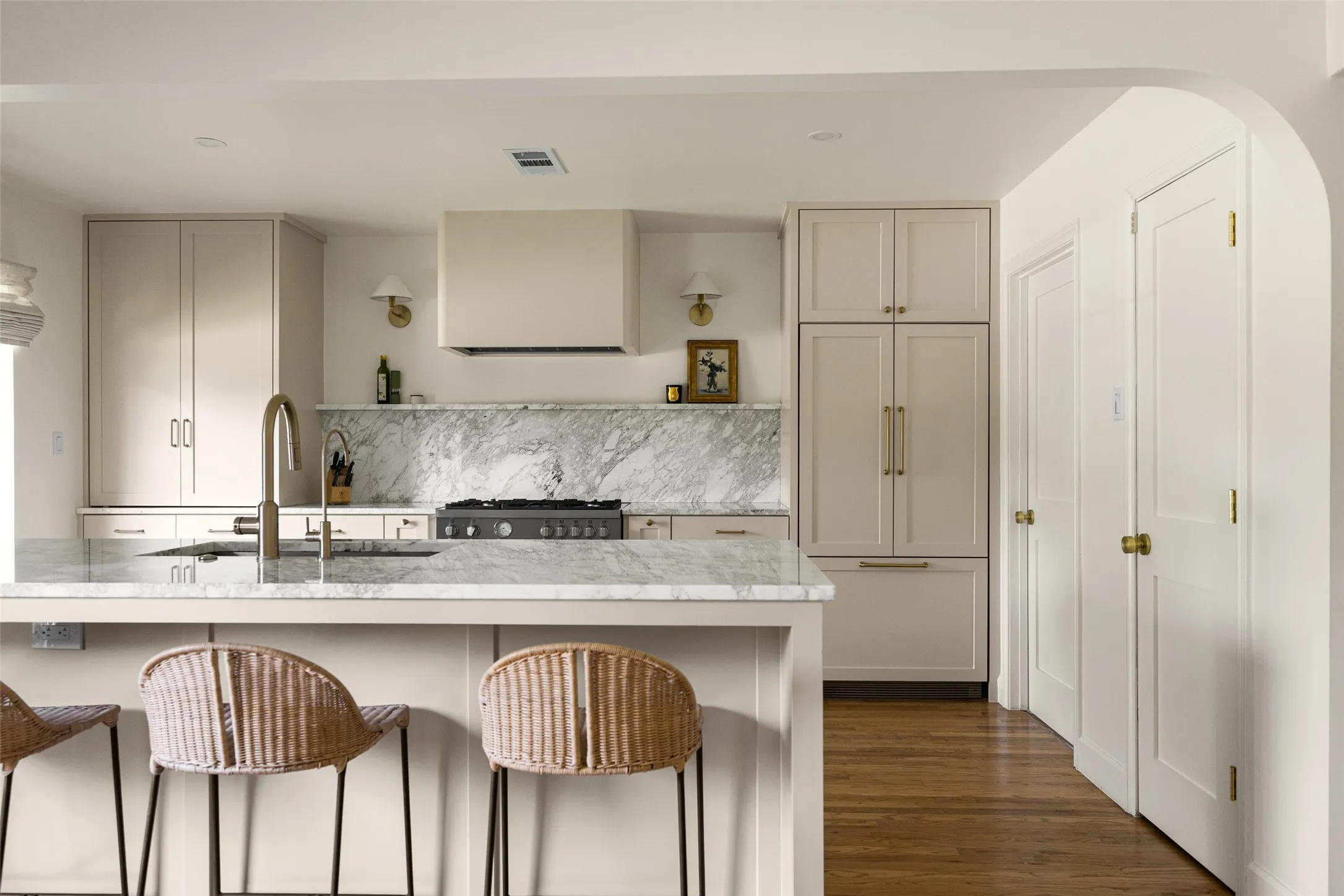 Kitchen featuring light-toned cabinetry, a large center island with a built-in sink, stone countertops and backsplash, a professional-grade range with a custom hood, and integrated refrigeration