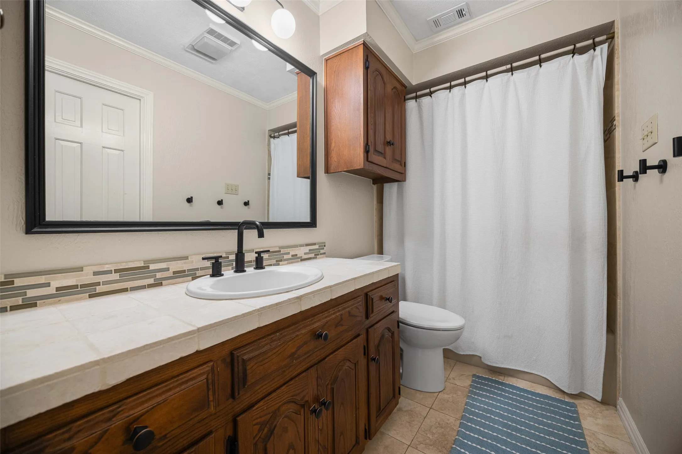 Bathroom vanity featuring a tiled countertop, undermount sink, matte black faucet, and a large framed mirror