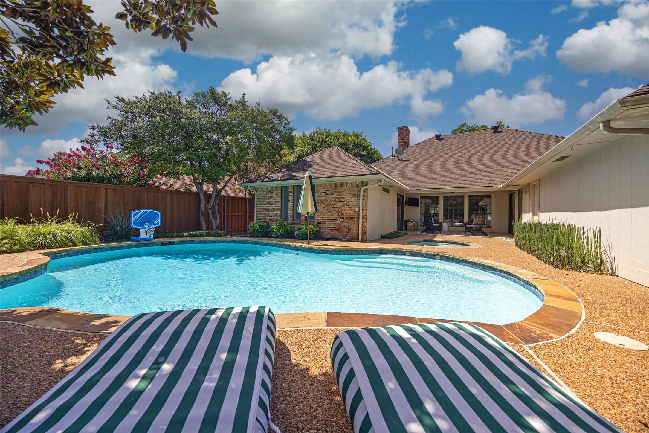 Outdoor swimming pool with a curved perimeter and integrated spa, surrounded by an exposed aggregate patio