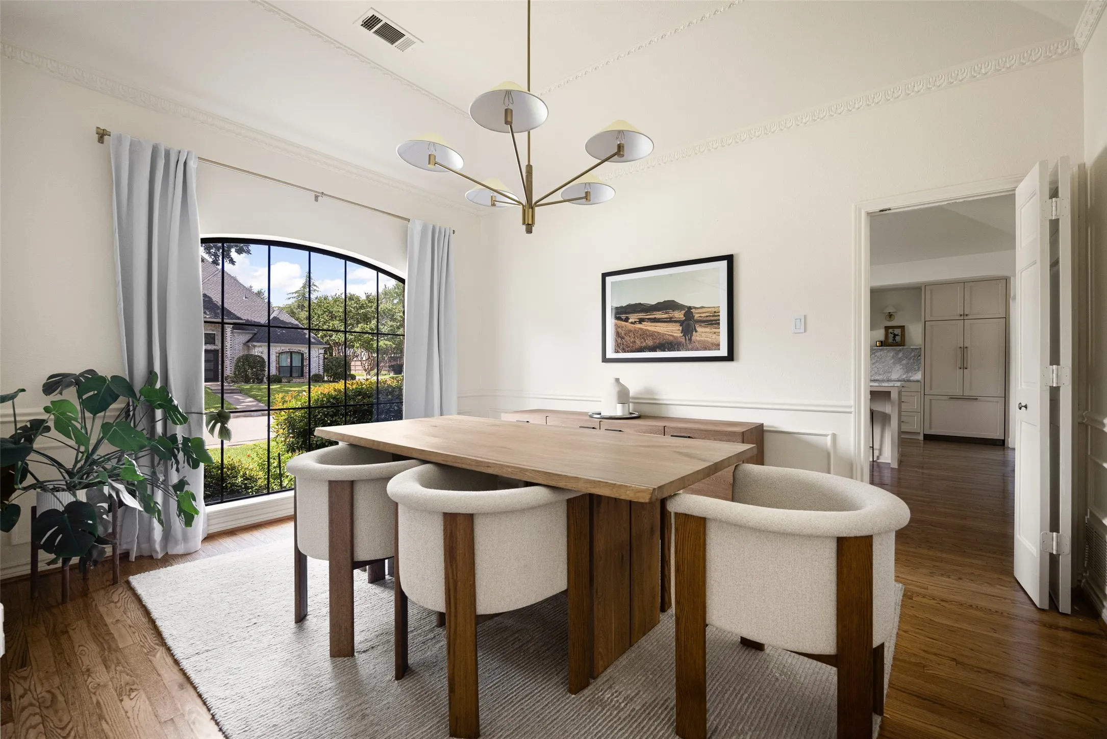 Dining area featuring an arched picture window, wood-finish flooring, crown molding, and wainscoting