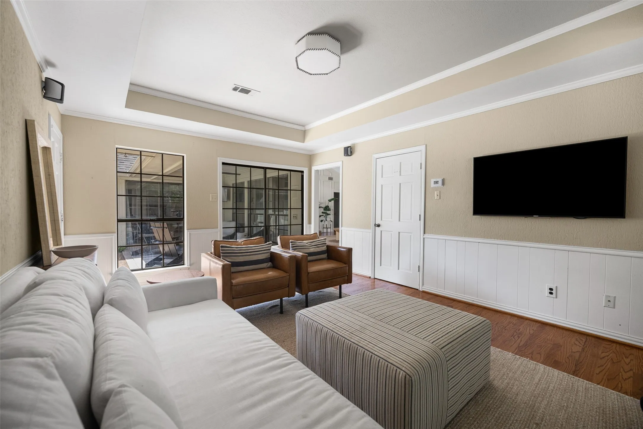 Living area featuring wood-finish flooring, white wainscoting, and a tray ceiling