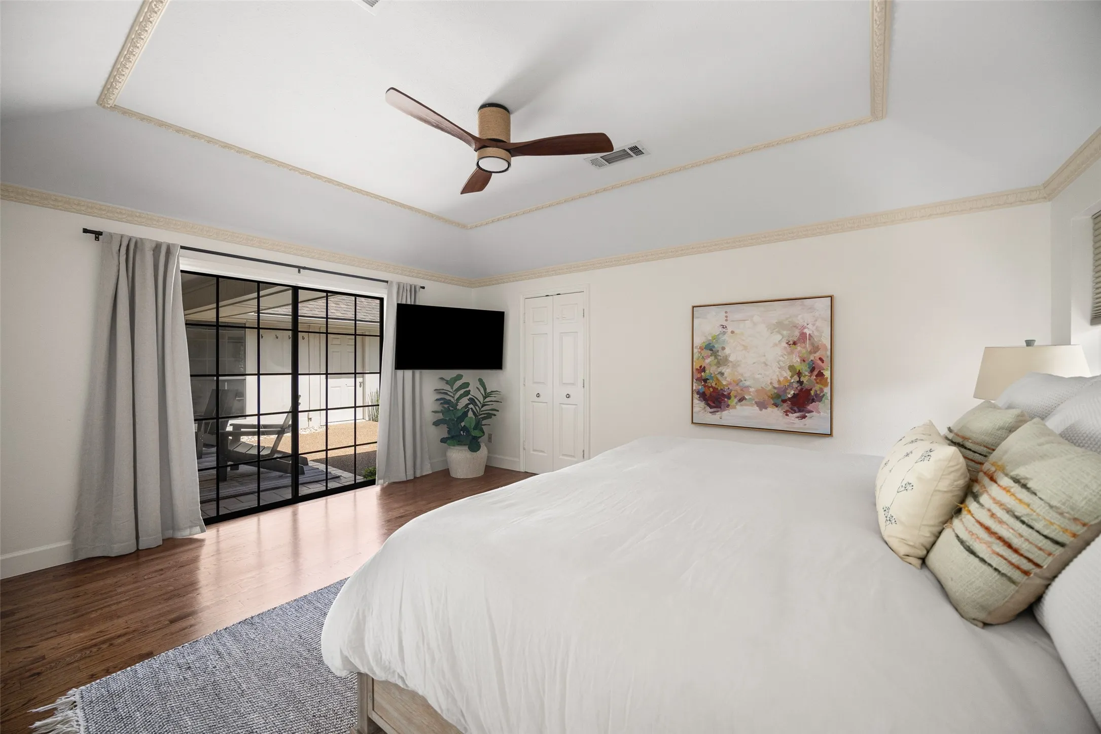 Tray ceiling with decorative molding, wood-finish flooring, and black-framed glass sliding doors leading to an outdoor space