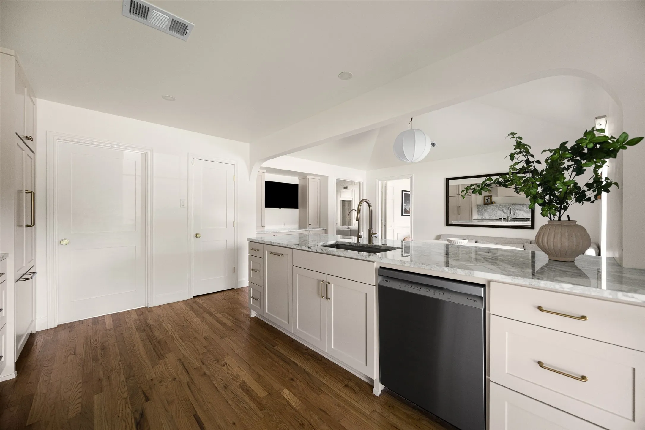 Kitchen island featuring a stainless steel sink with a gooseneck faucet, light-toned cabinetry, and a light-colored stone countertop