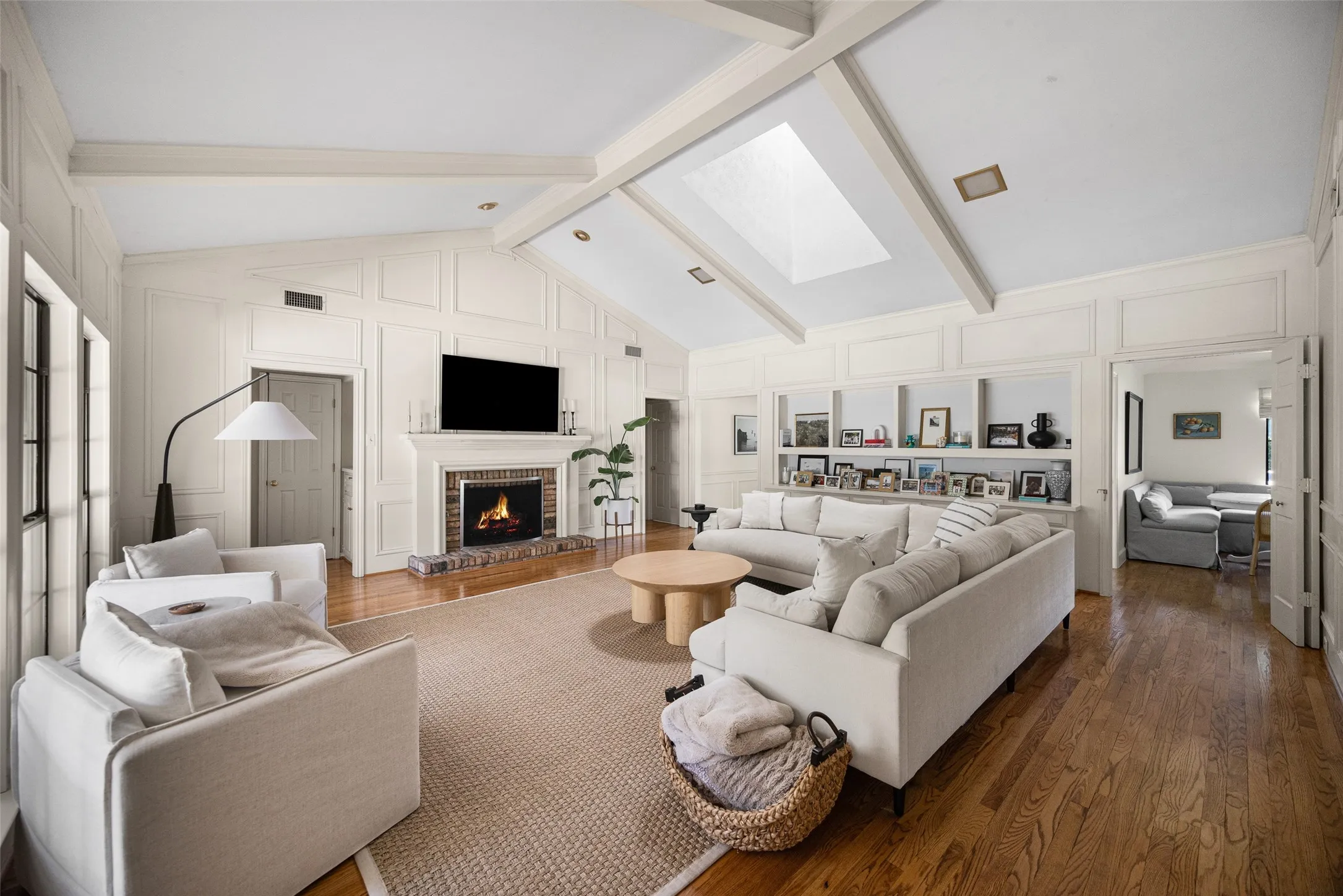 Spacious living area featuring a vaulted ceiling with exposed beams, skylight, and recessed lighting