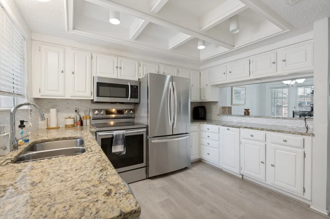 White cabinetry, stainless steel appliances, coffered ceiling, wood-finish flooring, and stone countertops