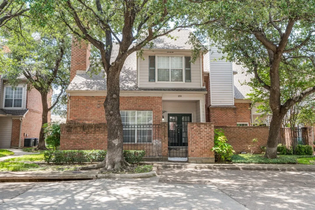 Brick and siding exterior with mature trees and a gated entry