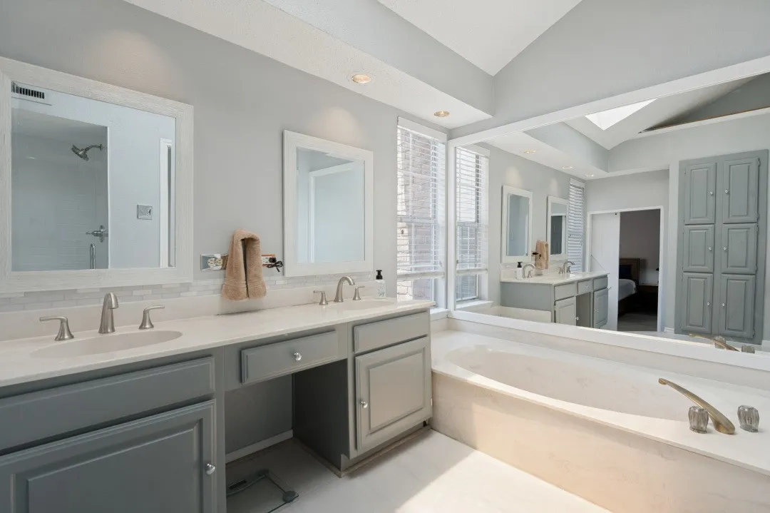Spa-inspired primary bathroom featuring dual vanities with gray cabinetry, white quartz countertops, and polished nickel fixtures