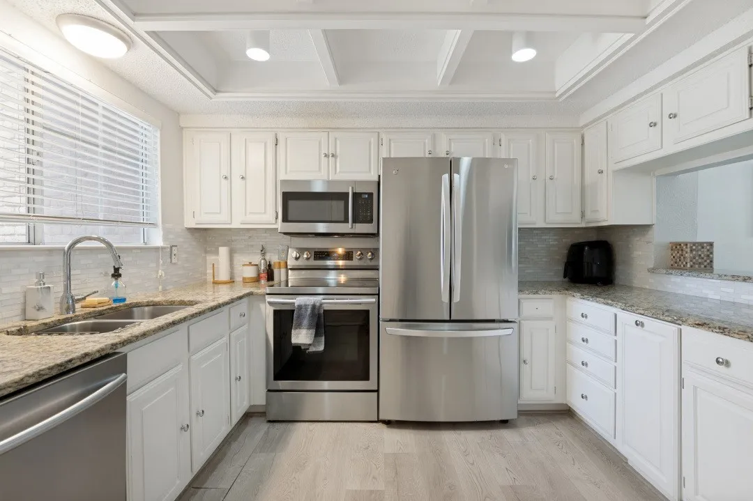 Modern kitchen featuring white cabinetry, stainless steel French-door refrigerator, and built-in stainless steel appliances including double wall oven and microwave