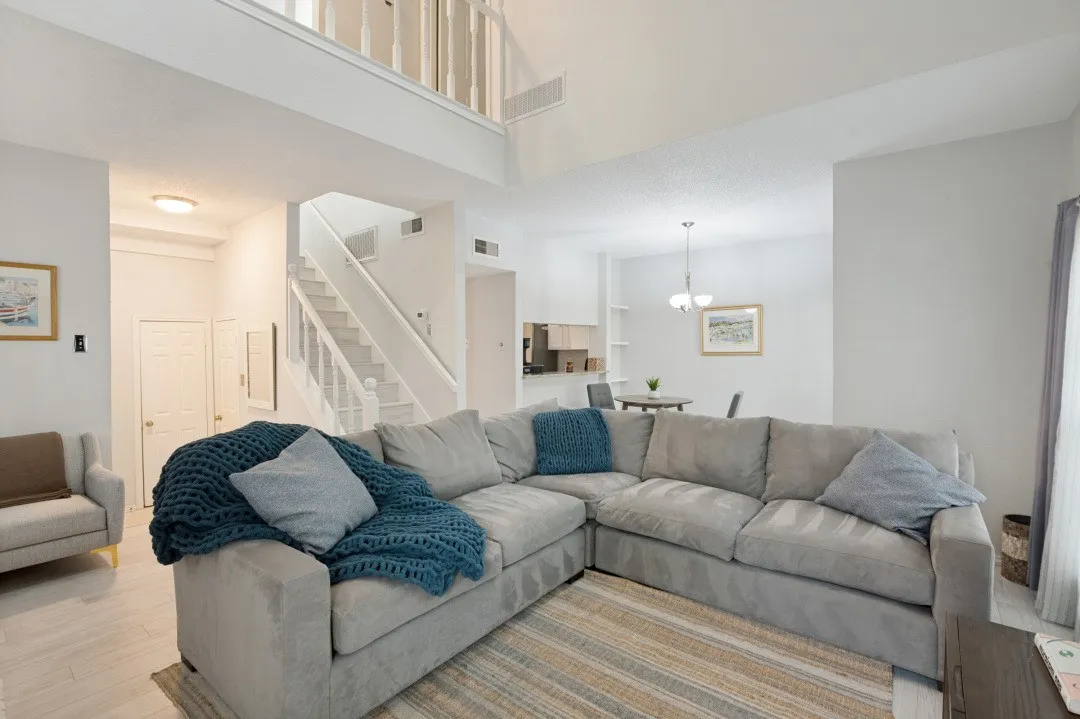 Vaulted ceiling with an upper-level railing, staircase with white newel posts, and wood-finish flooring